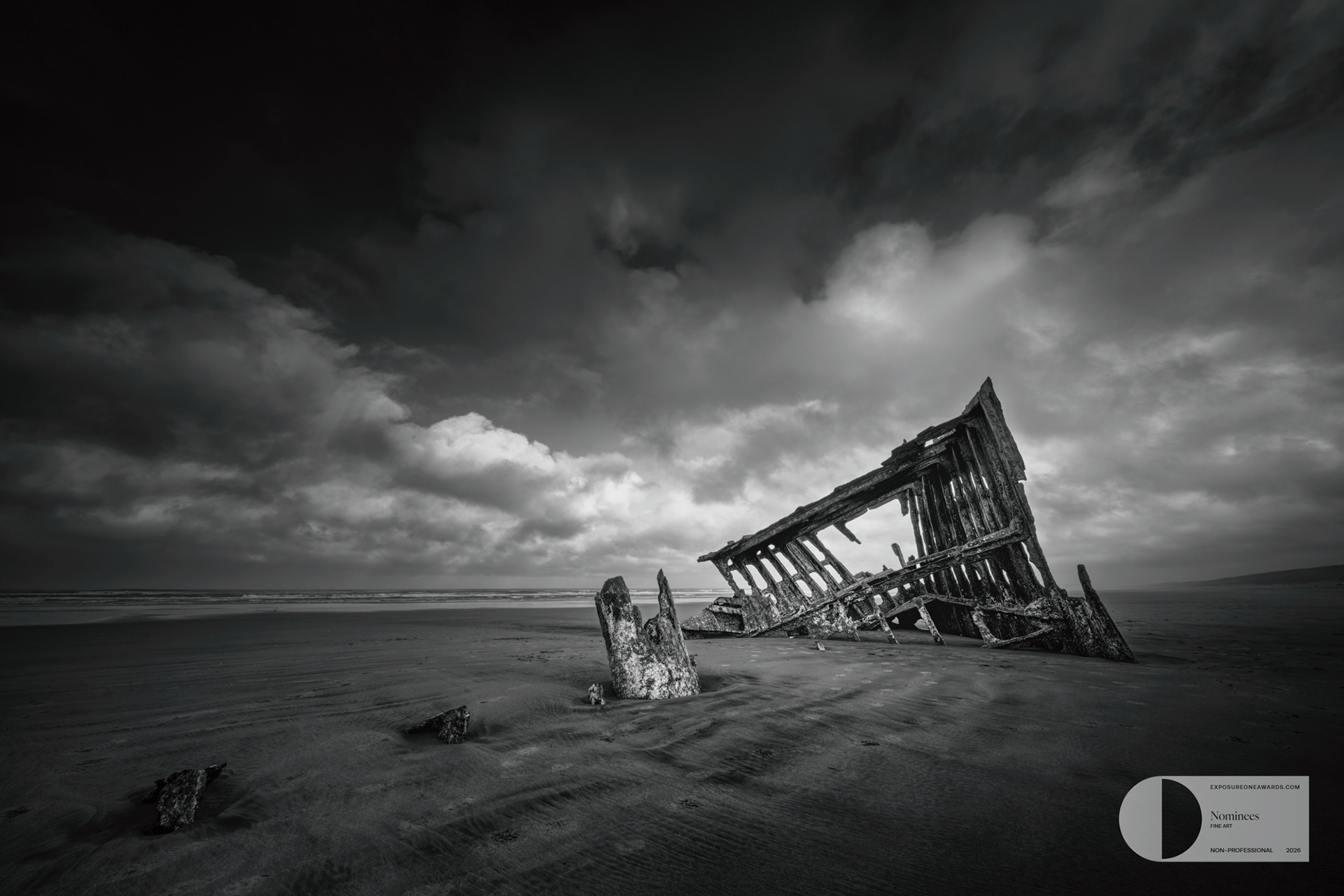 THE WRECK OF THE PETER IREDALE | The skeletal remains of the Peter Iredale lean into the sand beneath a turbulent sky, a quiet reminder of time, tide, and the sea’s final claim.