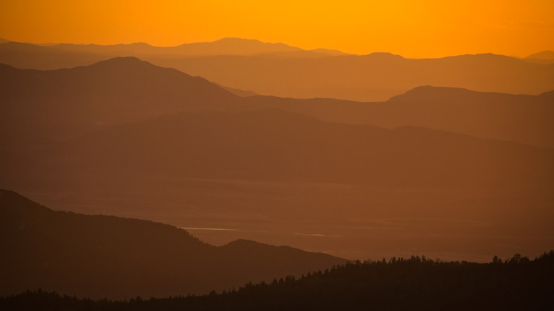 LAYERS OF SILENCE   |  Layer upon layer, ridge beyond ridge, the landscape dissolves into atmosphere. Mountains become silhouettes, silhouettes become shadows, and shadows fade into light. The scene is stripped of detail, leaving only shape, tone, and distance.Bathed in amber light, the image feels less like a photograph and more like a memory. The haze softens every edge, transforming the mountains into overlapping waves that drift toward the horizon. Each successive layer grows lighter and more ethereal, creating a remarkable sense of depth and scale.The simplicity is what gives the image its strength. There is no obvious focal point demanding attention. Instead, the eye wanders slowly through the composition, tracing the contours of ridges that emerge briefly before disappearing into the glow. The result is contemplative and calming, inviting the viewer to linger rather than simply observe.