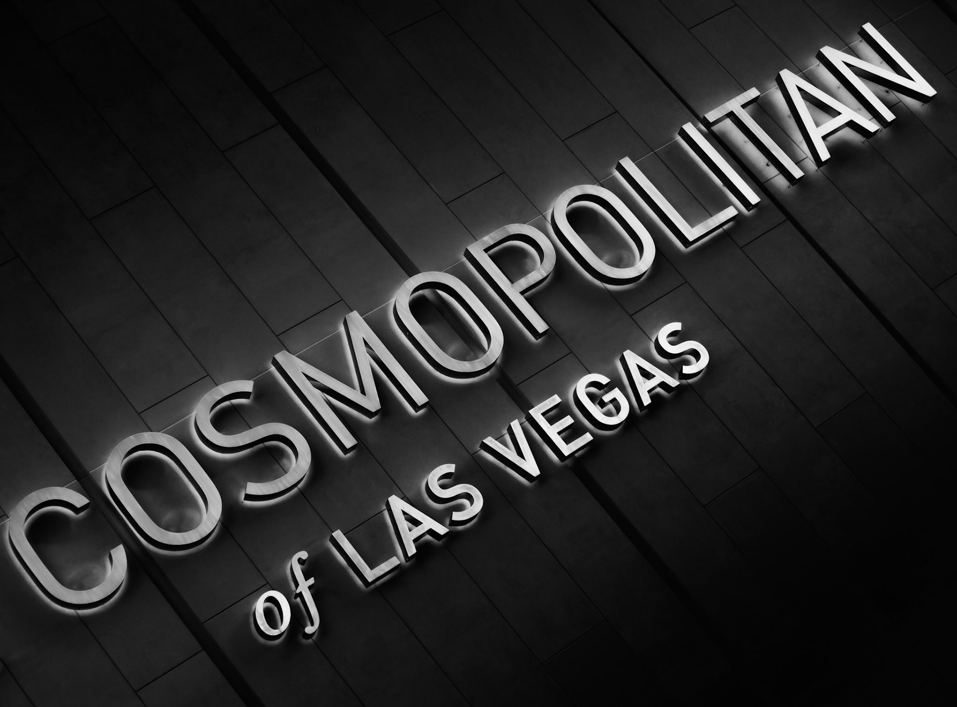 THE COSMOPOLITAN  |  The illuminated letters of the Cosmopolitan rise from a dark façade, transforming a simple hotel sign into a study of light, geometry, and contrast. The diagonal composition creates energy and movement, drawing the eye across the frame while emphasizing the modern design of the building.Presented in black and white, the image strips away the distractions of the Las Vegas Strip and focuses on form, texture, and typography. The glowing letters appear to float against the dark architectural surface, creating a minimalist interpretation of one of the city's most recognizable destinations.Rather than capturing the spectacle typically associated with Las Vegas, the photograph isolates a single graphic element, finding simplicity and elegance within a city known for excess.