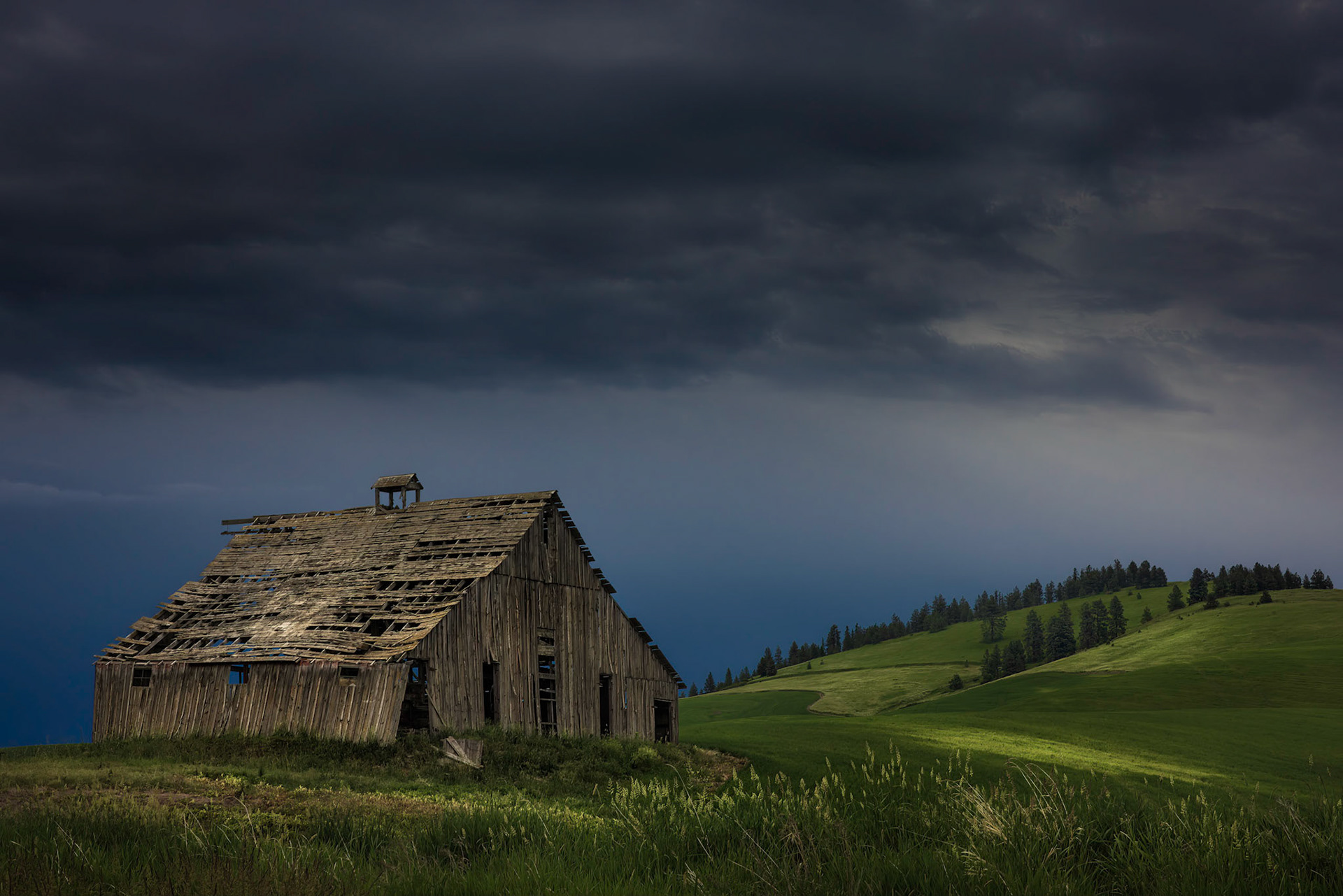 TATTERED BARN UNDER STORMY SKIES