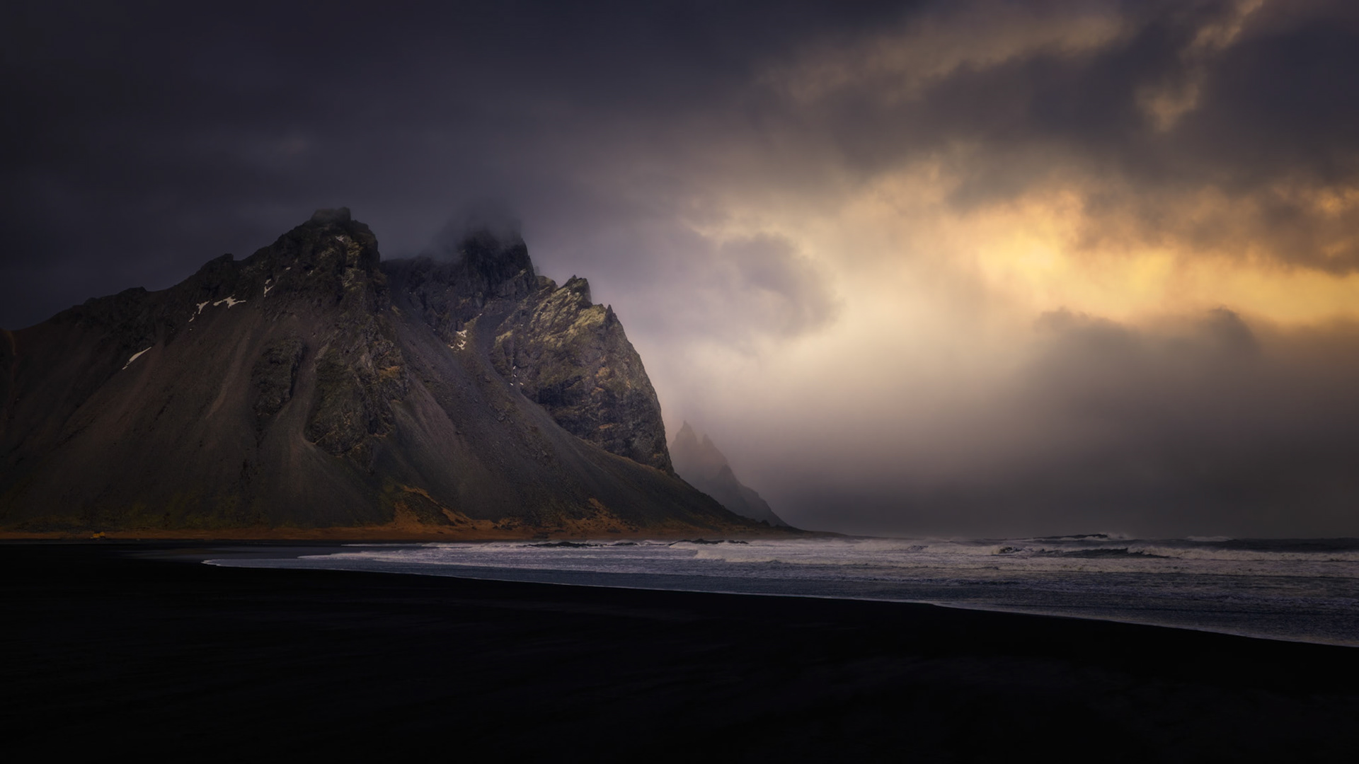 VEIL OF SHADOWS   |  Few places in Iceland possess the dramatic beauty of Vestrahorn. Rising sharply from the black sand beaches of the southeast coast, its jagged peaks create one of the country's most iconic and photogenic landscapes.On this morning, a passing storm transformed an already remarkable scene into something unforgettable. Dark clouds and rain swept across the mountain while a break in the weather allowed sunlight to spill through, illuminating the shoreline and sea in warm, golden light. The contrast between storm and sunshine lasted only moments, but it revealed the raw beauty that makes Iceland unlike anywhere else on Earth.Of all the landscapes I have photographed in Iceland, this remains one of my favorites. The combination of the black sand beach, the towering mountain, and the fleeting light breaking through the storm created a scene that was both powerful and breathtakingly beautiful.