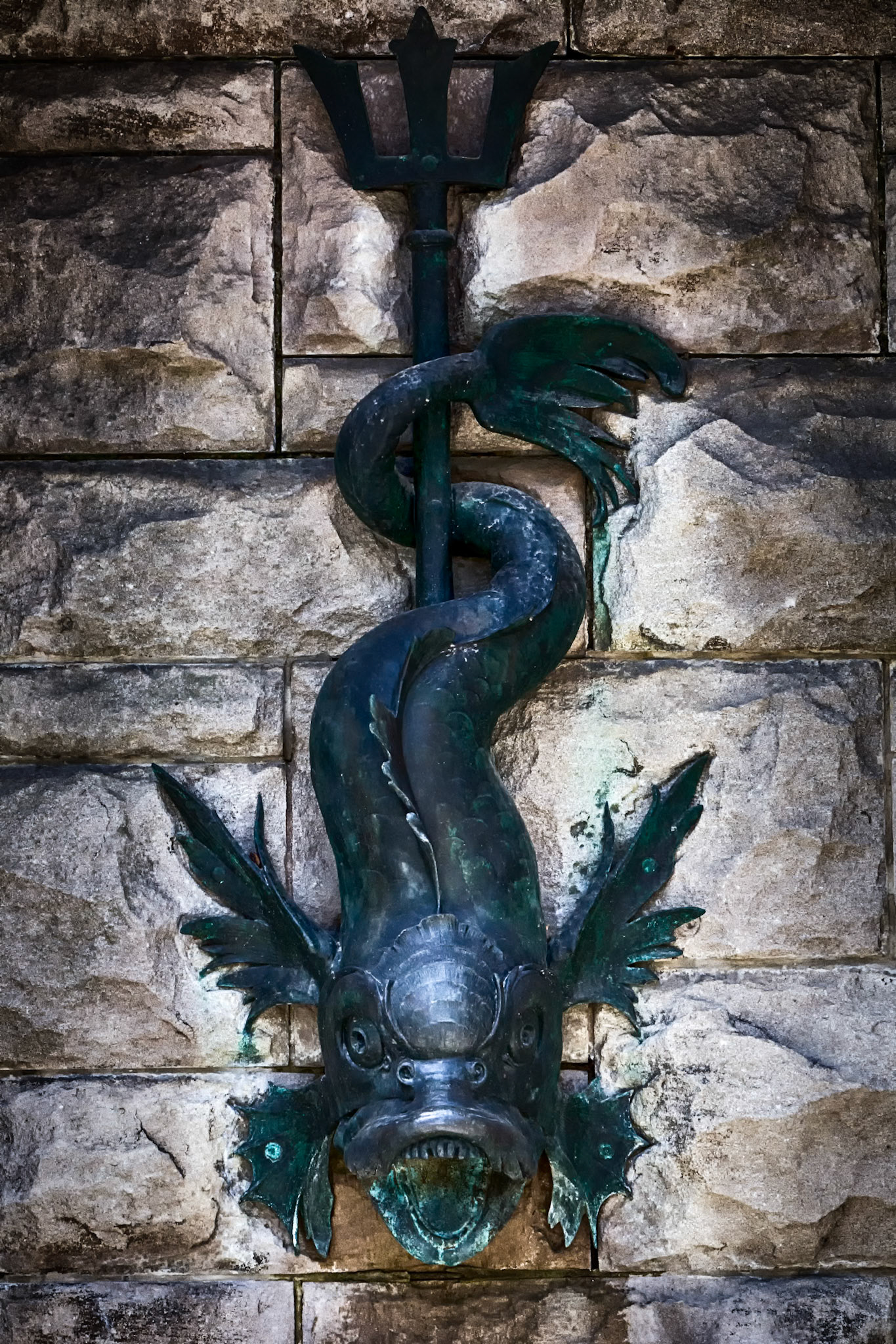 MYTH IN BRONZE  |  Mounted against the stonework of the Biltmore Estate, this bronze sea creature combines elements of fish, serpent, and dragon. Time and weather have softened its surface, creating a rich patina that contrasts with the textured masonry behind it.Originally designed as a decorative waterspout, the sculpture reflects the influence of European estates where mythology, architecture, and landscape were often woven together. Its exaggerated features and flowing form transform a practical architectural element into a work of art.Viewed up close, details that might otherwise go unnoticed become the focus. The curling body, open mouth, and stylized fins give the creature a sense of movement, as though it could emerge from the wall at any moment. The image highlights the craftsmanship and imagination found throughout the estate, where even the smallest architectural details were designed to leave a lasting impression.
