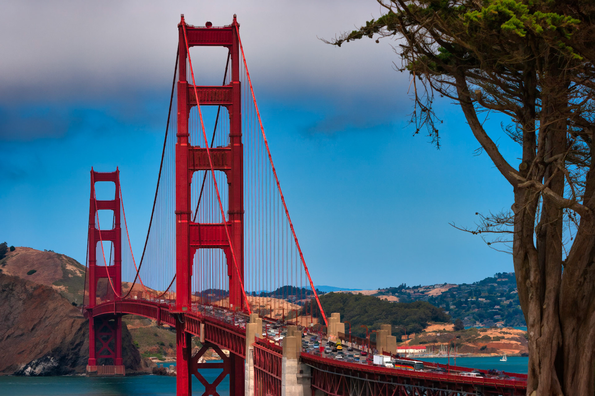 WHERE THE CITY CONNECTS  |  Even among the world's most photographed landmarks, the Golden Gate Bridge never loses its ability to command attention. Framed by wind shaped cypress and a dramatic sky, its towering red spans seem to rise from the landscape rather than cross it.A symbol of connection, resilience, and possibility, it remains as captivating today as when it first opened nearly a century ago.