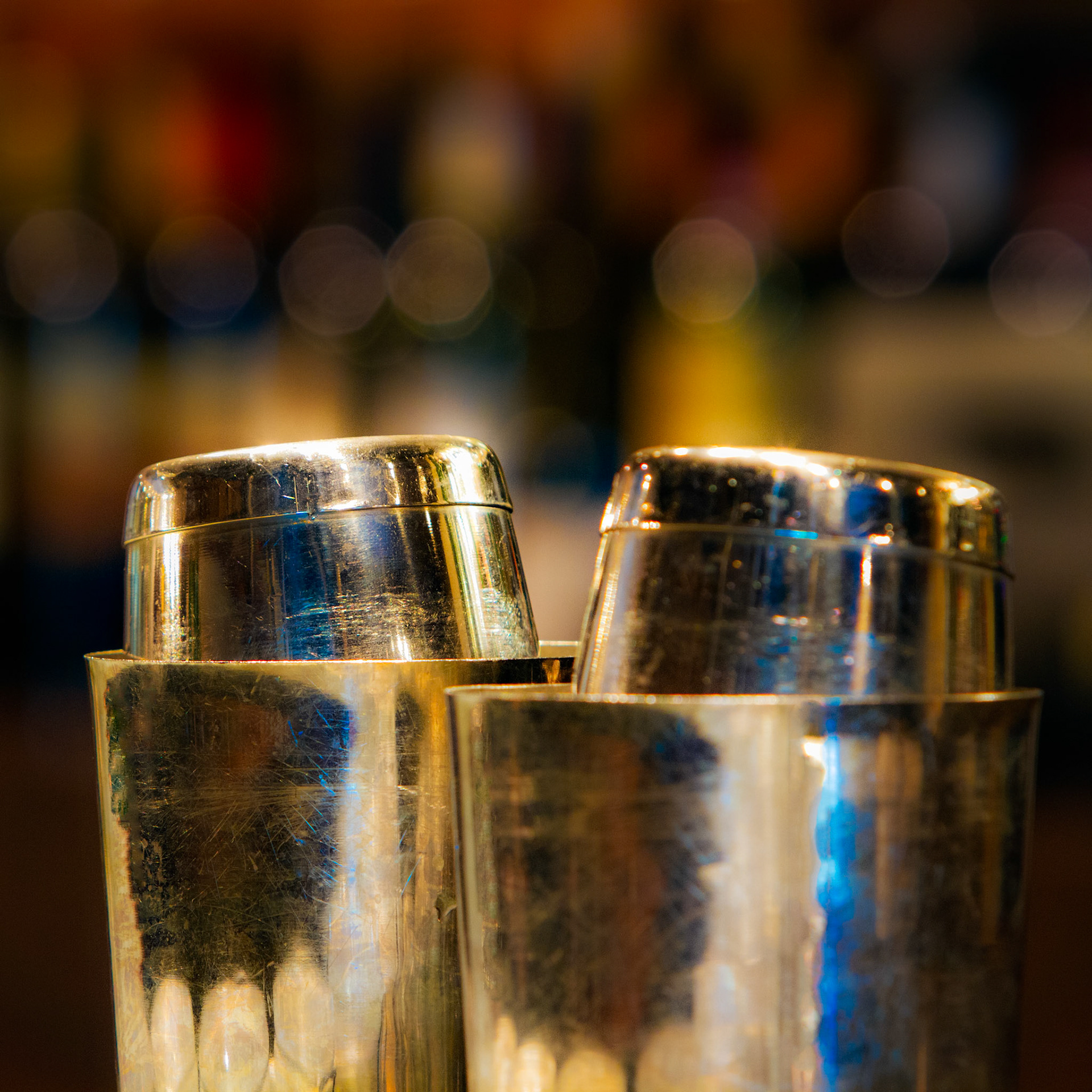 SHAKERS  |  The evening rush had not yet begun. Behind the bar, a pair of well worn cocktail shakers rested quietly, their scratched surfaces reflecting years of conversations, celebrations, and chance encounters. Every mark hinted at countless drinks prepared and stories shared.What drew me to the scene was not the shakers themselves, but the atmosphere surrounding them. The warm glow of the background dissolved into soft circles of light, transforming an ordinary moment into something more intimate. The image speaks to anticipation, that brief pause before the first order arrives or before the next story begins.Sometimes the most compelling subjects are not the people in a room, but the objects that silently witness everything.This image celebrates the beauty hidden in everyday rituals and the quiet elegance of craftsmanship shaped by use.