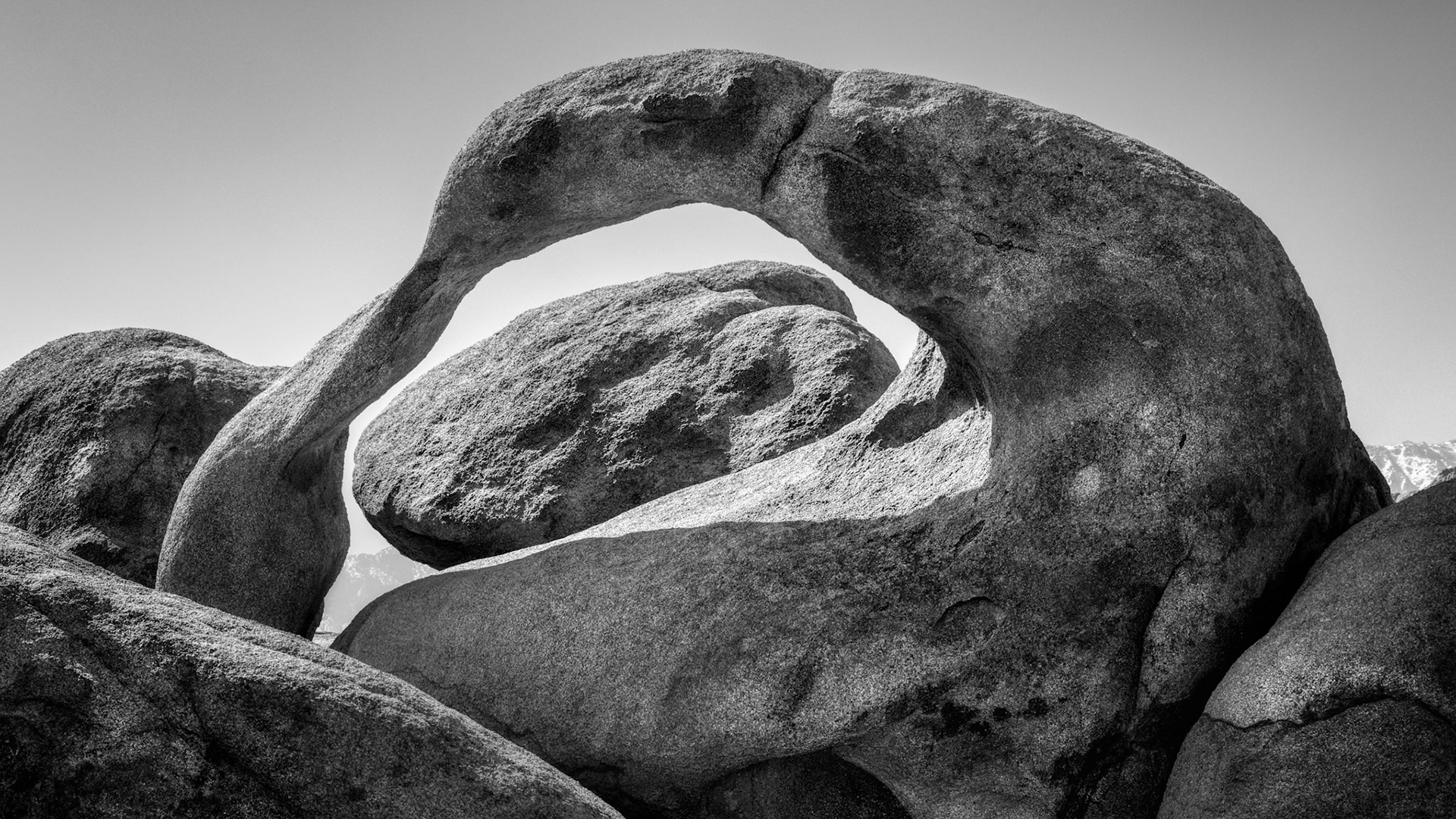 STONE IN BALANCE  |  In a landscape defined by extremes, this graceful arch feels almost impossible.Surrounded by massive granite boulders and the harsh beauty of the desert, nature somehow carved a shape that appears delicate, elegant, and surprisingly human. The sweeping curve seems less like stone and more like an arm reaching across time, embracing the ancient rocks that surround it.I was drawn to the simplicity of the scene. No dramatic skies. No colorful sunset. Just form, texture, shadow, and light.Black and white felt like the natural choice.Without color competing for attention, the viewer can appreciate the smooth contours sculpted by countless centuries of wind, water, temperature, and patience. Every crack, curve, and surface tells a story measured not in years, but in geologic time.Standing before it, I was reminded that some of nature's most beautiful creations are not the largest or most famous. They are the quiet details hidden among the grand landscapes, waiting for someone to notice.This arch may seem permanent, but it is only a moment in an ongoing process of creation and erosion. Someday it too will disappear.For now, it stands as a reminder that even stone can possess grace.
