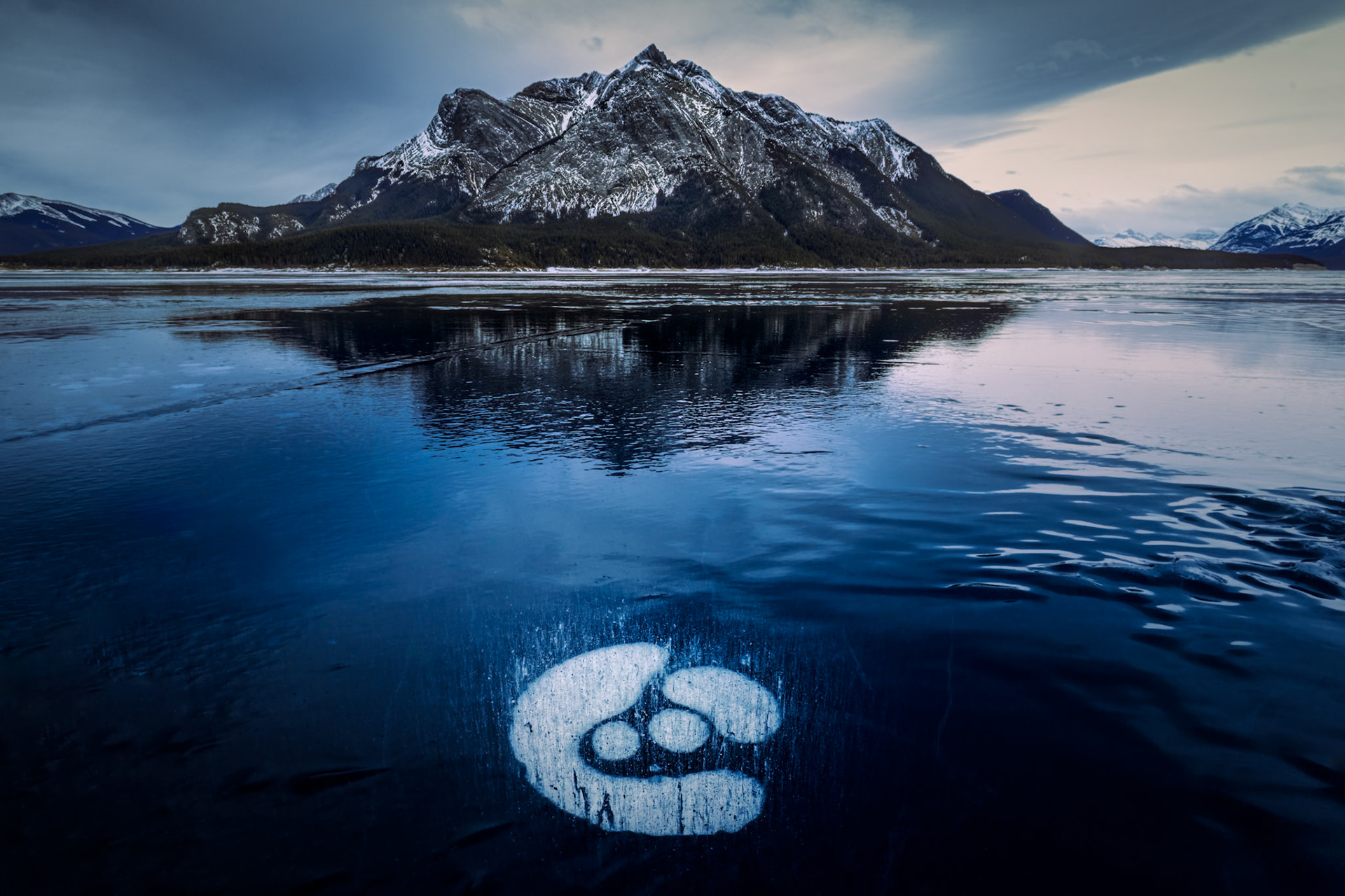 TRAPPED BREATH  |  Part of the magic of Abraham Lake lies in the discoveries that appear beneath your feet. While many visitors focus on the sweeping mountain views, I often found myself looking down, searching the ice for unusual patterns created by trapped methane bubbles.This formation immediately caught my attention because it seemed almost intentional. Encased within the deep blue ice, the bubbles gathered into a shape that felt more like a symbol or celestial arrangement than a natural occurrence. Surrounded by the vast frozen lake and the towering Rockies beyond, it became a reminder that some of nature's most fascinating details are found in the smallest corners of the landscape.What makes these formations so compelling is that no two are ever alike. Each winter, the lake creates a temporary gallery of abstract designs that exist for only a short season before thawing away. This image preserves one of those fleeting moments, hidden in plain sight beneath the frozen surface.