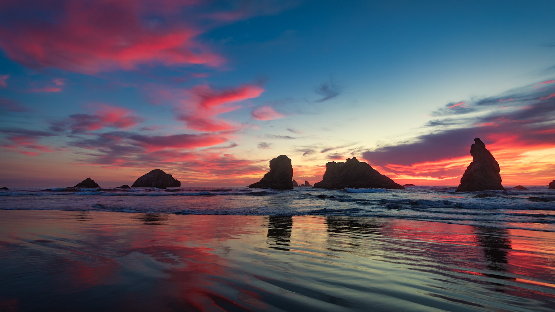 EMBERS OVER BANDON  |  As the sun slips below the horizon, the sky above Bandon Beach erupts in brilliant shades of crimson, magenta, and gold. Reflected across the wet sand and rolling tide, the colors transform the shoreline into a mirror of the evening sky.The iconic sea stacks rise from the Pacific as dark silhouettes, their timeless forms anchoring a scene that feels almost otherworldly. For a few fleeting minutes, the ocean, sky, and land become inseparable, each reflecting the beauty of the other.Some sunsets are beautiful. Others are unforgettable. This image captures one of those rare moments when nature seems determined to put on its finest display, leaving those fortunate enough to witness it standing quietly in awe.