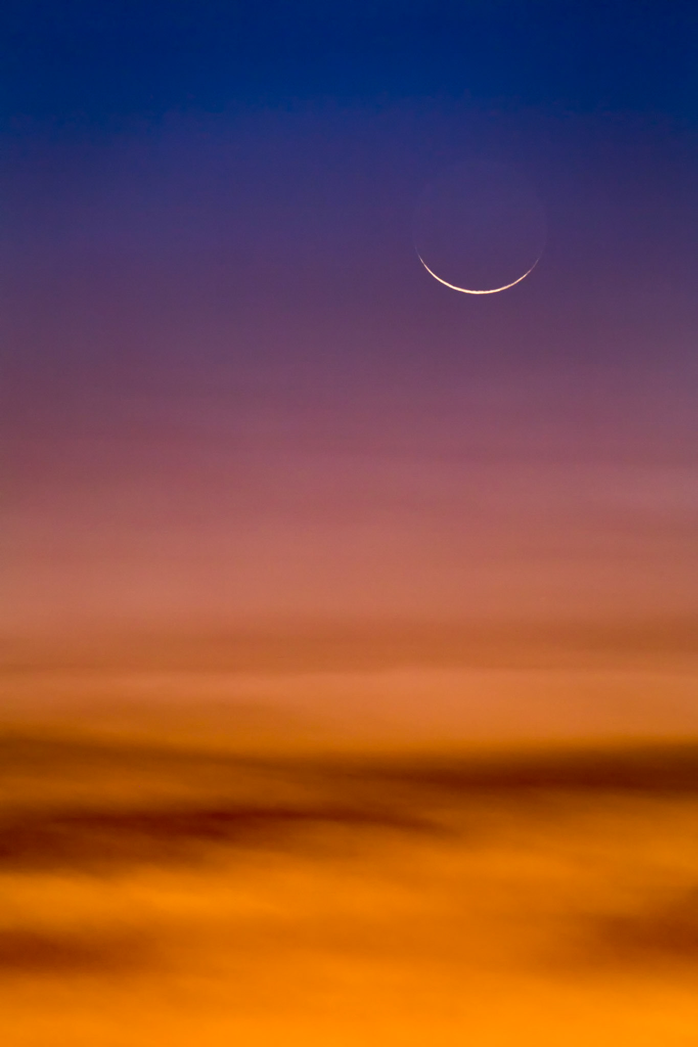 QUIET CRESCENT  |  A slender crescent moon hangs delicately above a sea of glowing clouds, suspended between the fading warmth of sunset and the deepening blue of night.