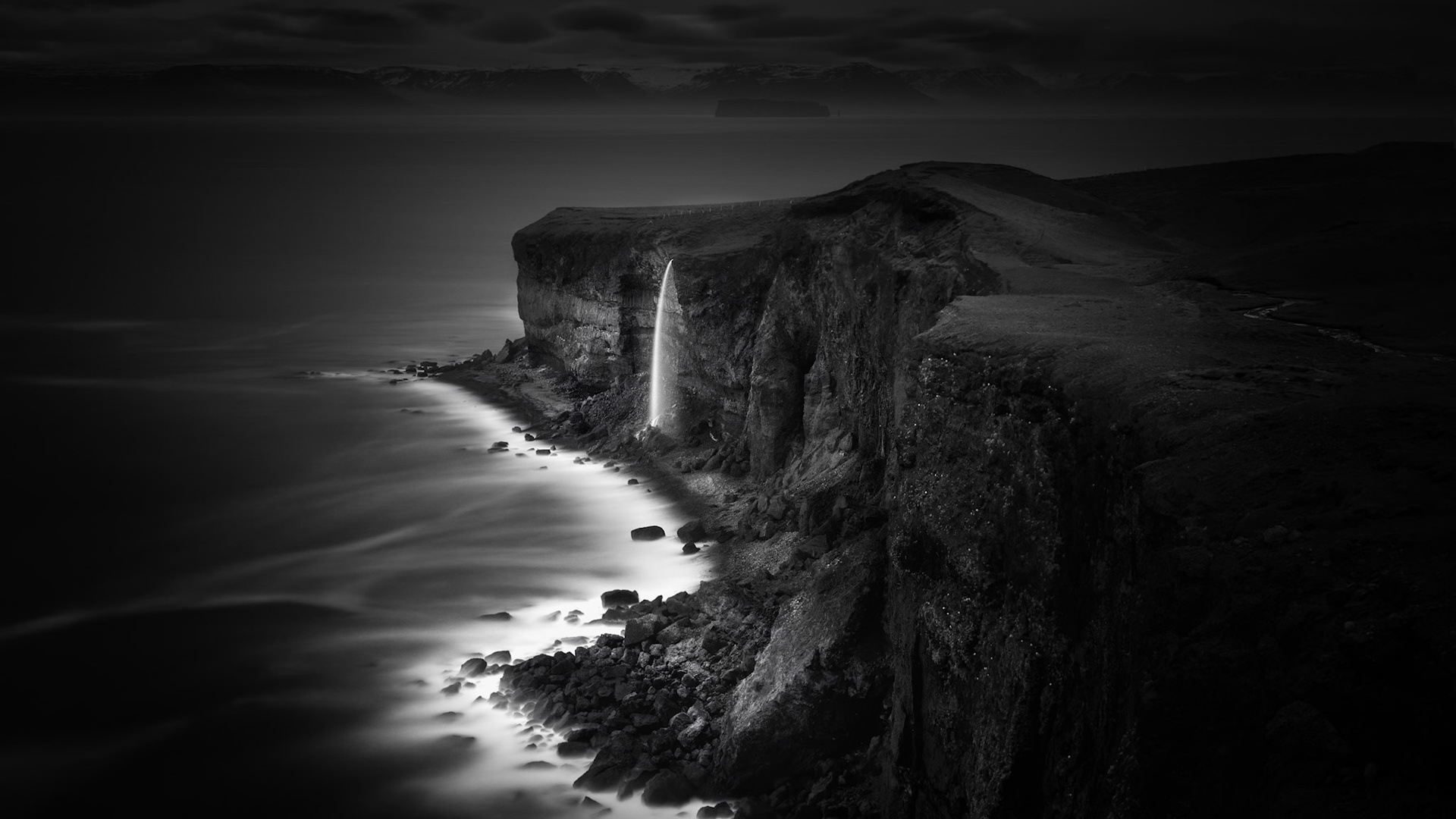 FALLS INTO THE SEA  |  Along the rugged coastline of northern Iceland, a solitary waterfall spills from towering sea cliffs into the waters below, creating a scene of remarkable beauty and solitude. Far from crowds and carved by centuries of wind, ice, and ocean storms, the landscape feels untouched by time.