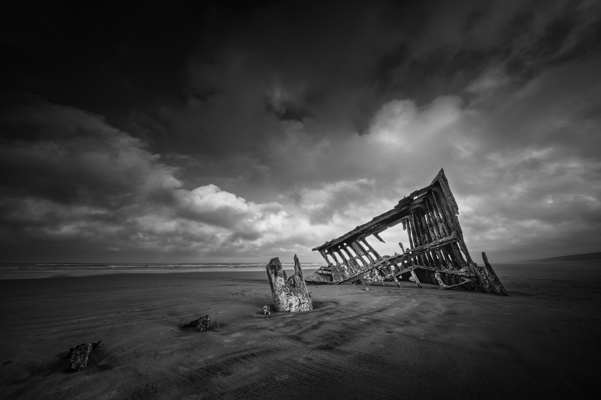 THE WRECK OF THE PETER IREDALE | The skeletal remains of the Peter Iredale lean into the sand beneath a turbulent sky, a quiet reminder of time, tide, and the sea’s final claim.