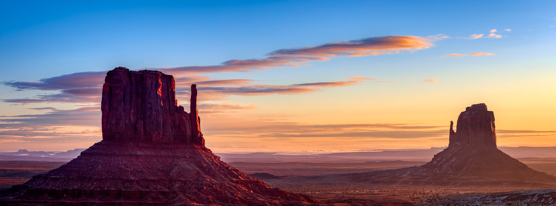 RED GIANTS  |  Some landscapes are so iconic that they feel familiar long before you ever arrive. Monument Valley was one of those places for me.Yet standing there before sunrise, wrapped against the desert cold and watching the first light touch the East and West Mittens, I realized no photograph, movie, or postcard can prepare you for the real thing.As dawn approached, the valley slowly emerged from darkness. The sandstone buttes, carved by millions of years of erosion, stood like ancient guardians over the desert floor. Then, almost imperceptibly, the rising sun began to paint their faces with warm crimson light while the surrounding landscape remained cloaked in shadow.For a few brief minutes, the Mittens seemed to glow from within.The scene carried an unexpected stillness. No crowds. No traffic. No distractions. Just the quiet transition between night and day across one of the most recognizable landscapes in the American West.The Navajo people call this place home, and it is easy to understand why this land inspires such reverence. The scale is immense, the silence profound, and the beauty timeless.Watching the sun rise between these legendary formations felt less like witnessing a sunrise and more like witnessing a ritual that has repeated itself for countless generations.A new day had begun, but the valley remained unchanged.