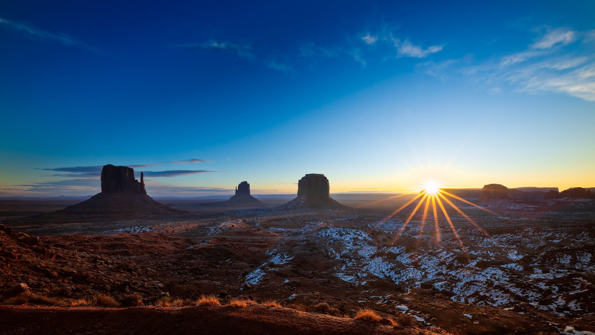 THE LONG AWAKENING  |  Some landscapes are beautiful. Others are iconic.Monument Valley belongs to the latter.Long before sunrise, I stood in the cold desert darkness waiting for the first hint of light. The towering sandstone buttes were little more than silhouettes against the horizon, their familiar shapes emerging slowly from the night.Then it happened.The sun crested the distant horizon and sent a burst of light across the valley floor. For a few fleeting moments, the desert awakened. Snow left behind by a recent storm caught the warm glow of morning, creating a striking contrast between winter's cool touch and the desert's timeless red earth.What makes Monument Valley so special is not simply its beauty, but its scale. These monumental formations rise hundreds of feet above the valley floor, standing as silent witnesses to millions of years of geological change. They have watched countless sunrises and sunsets, yet each new day feels as though it is being revealed for the very first time.Standing there, camera in hand, it was impossible not to feel small.The landscape stretched endlessly in every direction, while the rising sun transformed stone, snow, and sky into a scene that felt both ancient and eternal.Some places leave an impression.Monument Valley leaves a memory.