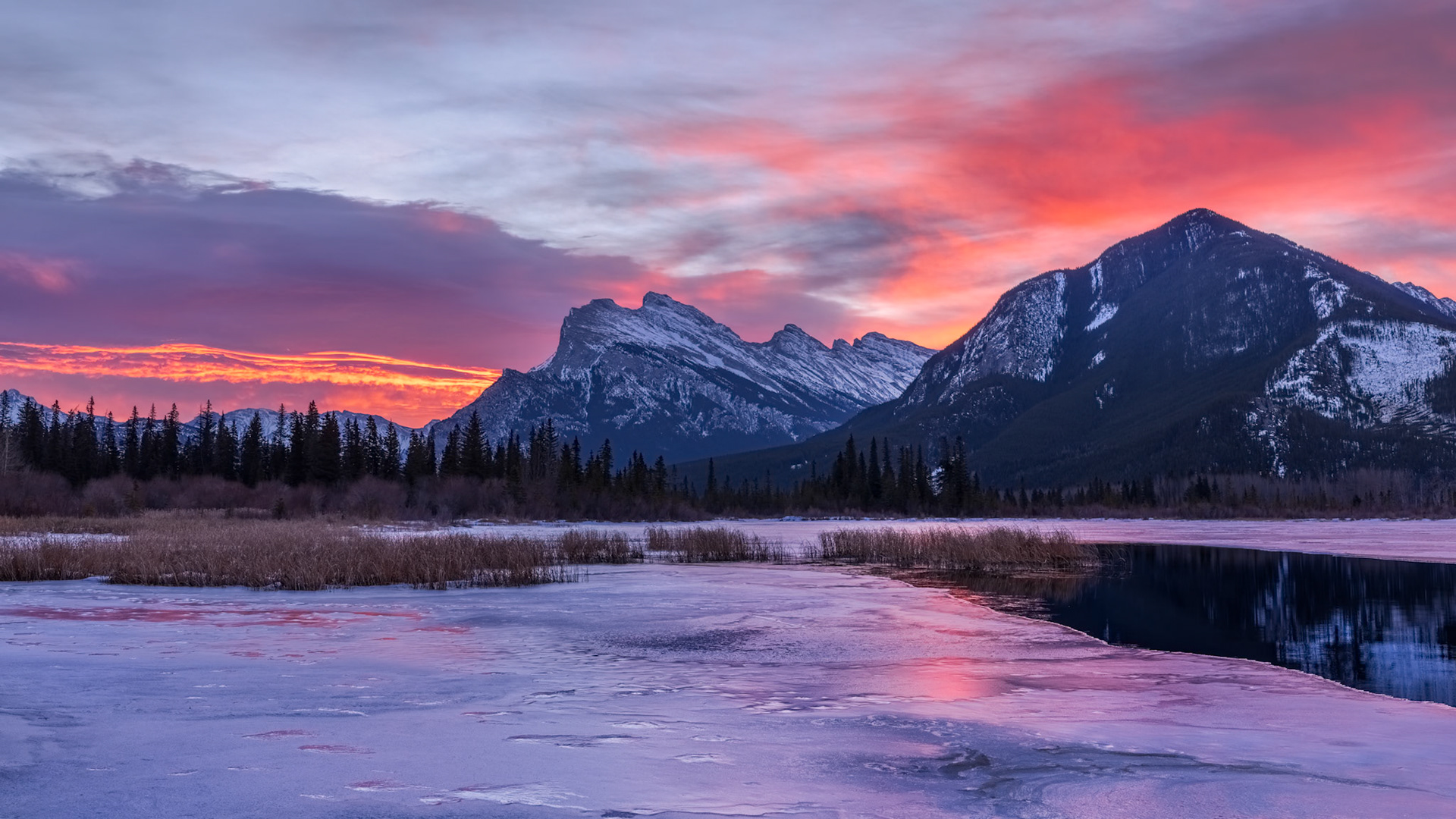 WHEN WINTER HOLDS THE LIGHT | Winter mornings in the Canadian Rockies often begin quietly, but occasionally the sky has other plans. This sunrise outside Banff unfolded in a matter of minutes, transforming a frozen landscape into a canvas of color. The mountains stood unchanged, as they have for millennia, while ribbons of crimson, magenta, and gold swept across the sky and reflected in the still water below.