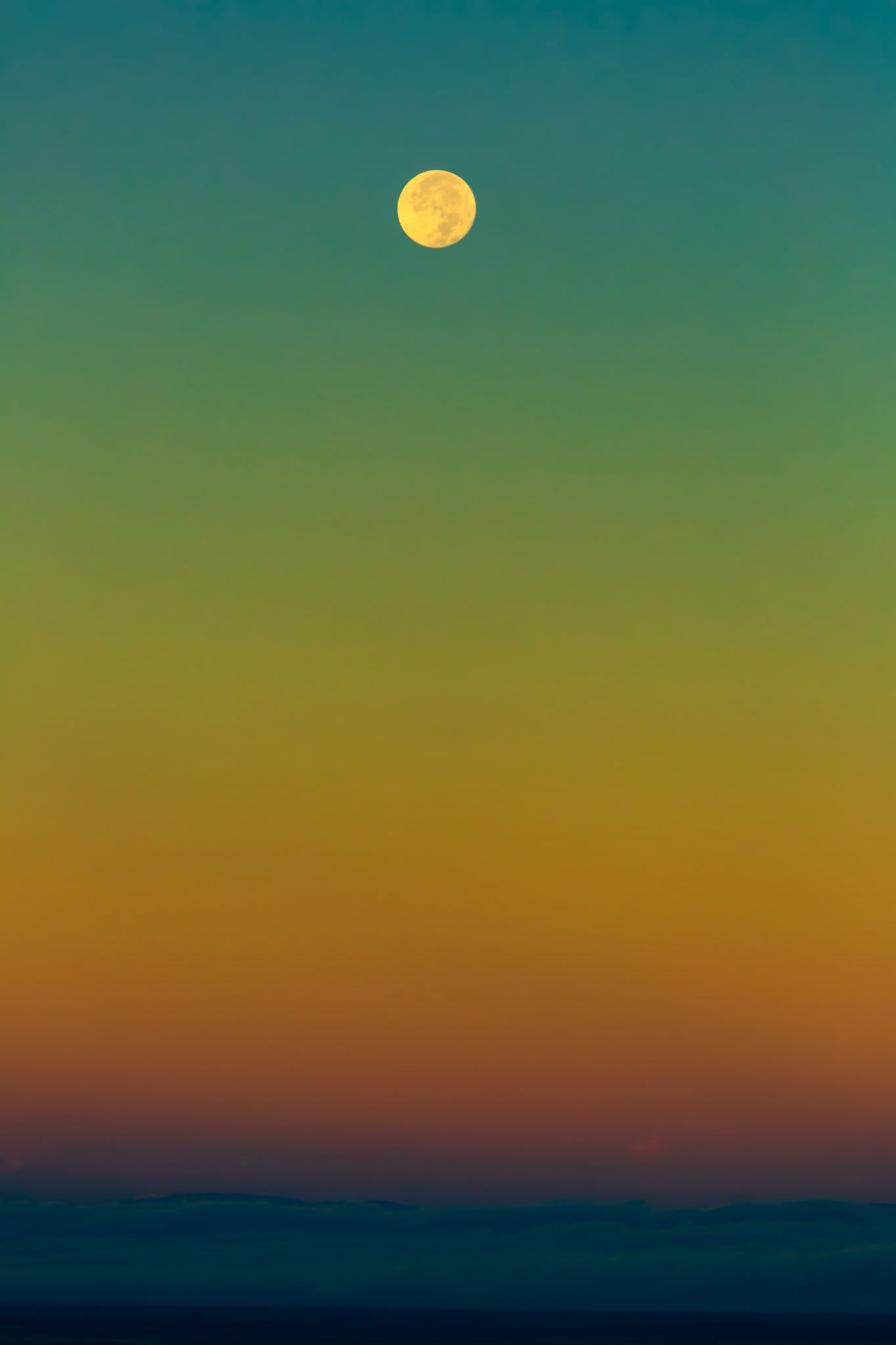 WEIGHTLESS  |  Suspended above a horizon of distant dunes and shadowed ridges, the full moon hangs in a sky painted with an extraordinary spectrum of color. Cool turquoise fades into emerald, then amber and violet, creating a natural gradient that feels almost dreamlike in its simplicity.Taken near Great Sand Dunes National Park, this image captures one of those fleeting moments when the earth, sky, and moon seem perfectly balanced. The vastness of the landscape is suggested rather than revealed, allowing the eye to linger on the delicate transition of color and the quiet presence of the moon.There is a sense of stillness here that invites reflection. As night yields to day, the moon makes its final descent while the sky awakens around it. The result is a scene that feels both expansive and intimate, reminding us that beauty often lies not in what dominates the frame, but in the space between.