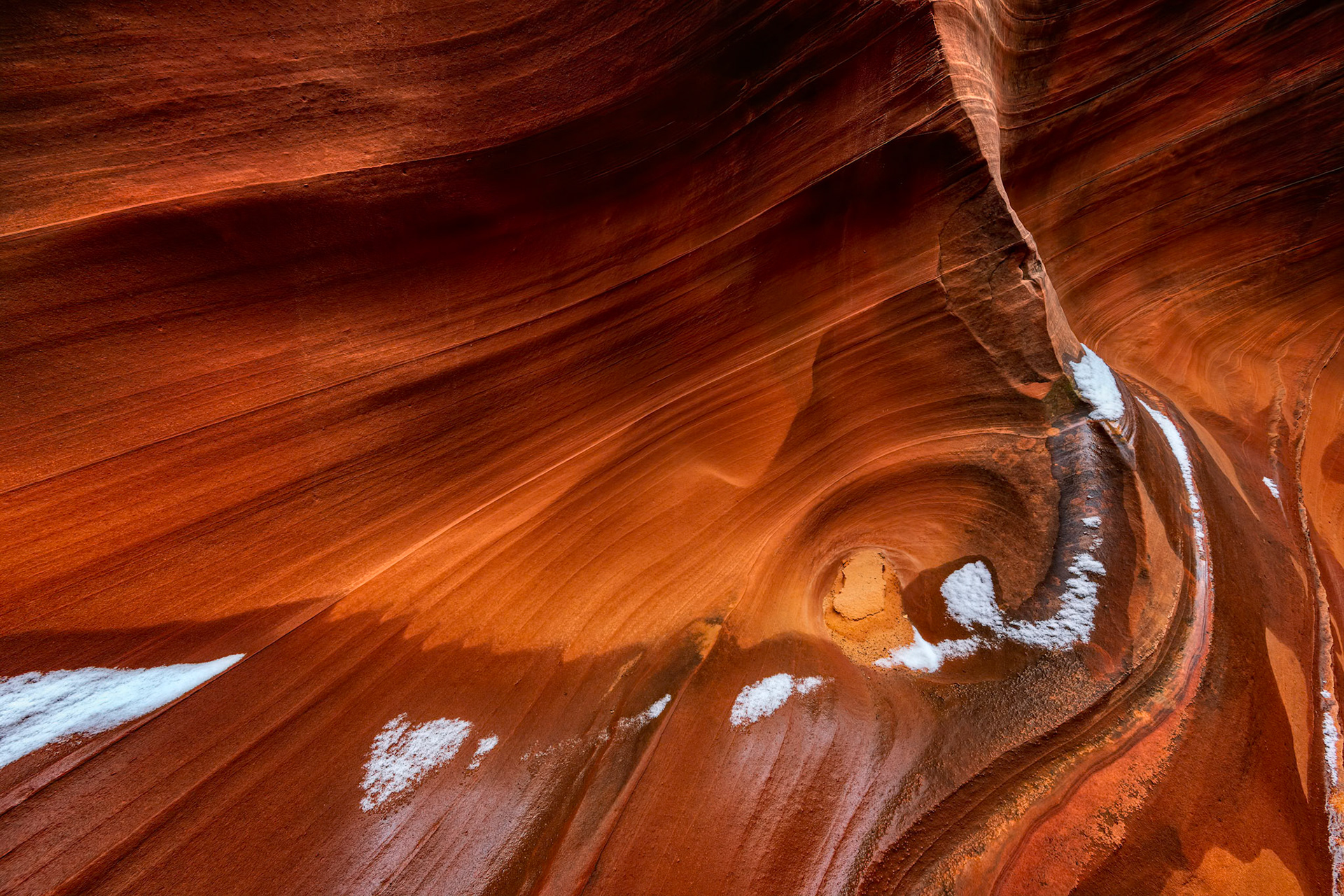 SANDSTONE SWIRL  |  Deep within Cardiac Canyon, the sandstone seemed almost alive.Over countless centuries, wind and water sculpted these flowing curves into shapes that feel more like silk than stone. Every surface twists, bends, and sweeps into the next, creating a natural sculpture that changes with every step and every shift of light.What stopped me in my tracks was not the canyon itself, but the snow.A recent winter storm had left delicate patches of white resting along the canyon walls, as if nature had carefully placed them there by hand. Against the rich reds and oranges of the Navajo sandstone, the snow became something more than a seasonal visitor. It felt like a gentle kiss, accenting the graceful swirl at the heart of the composition without distracting from it.The contrast was fleeting. Within days, perhaps hours, the snow would disappear, leaving only the timeless curves behind. Yet for one brief moment, winter and stone shared the same canvas, transforming an already extraordinary landscape into something even more magical.It was a reminder that some of nature's most beautiful moments are also its most temporary.