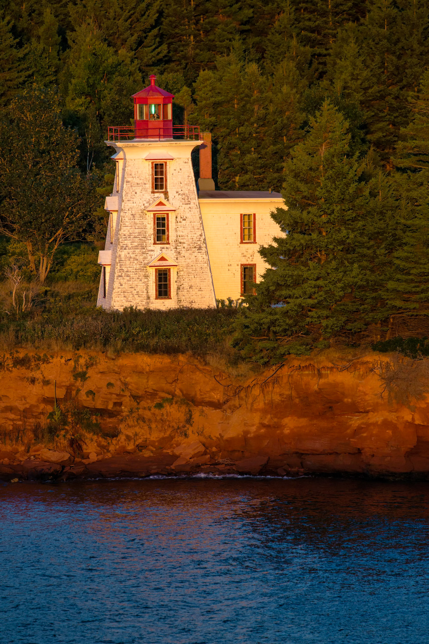 SENTINEL OF THE POINT  |  Bathed in the warm glow of the setting sun, this solitary lighthouse stands watch along the rugged coast of Nova Scotia. Surrounded by forest and perched above the rocky shoreline, it serves as a quiet reminder of the mariners who once relied on its beacon to guide them safely home through the waters of the North Atlantic.