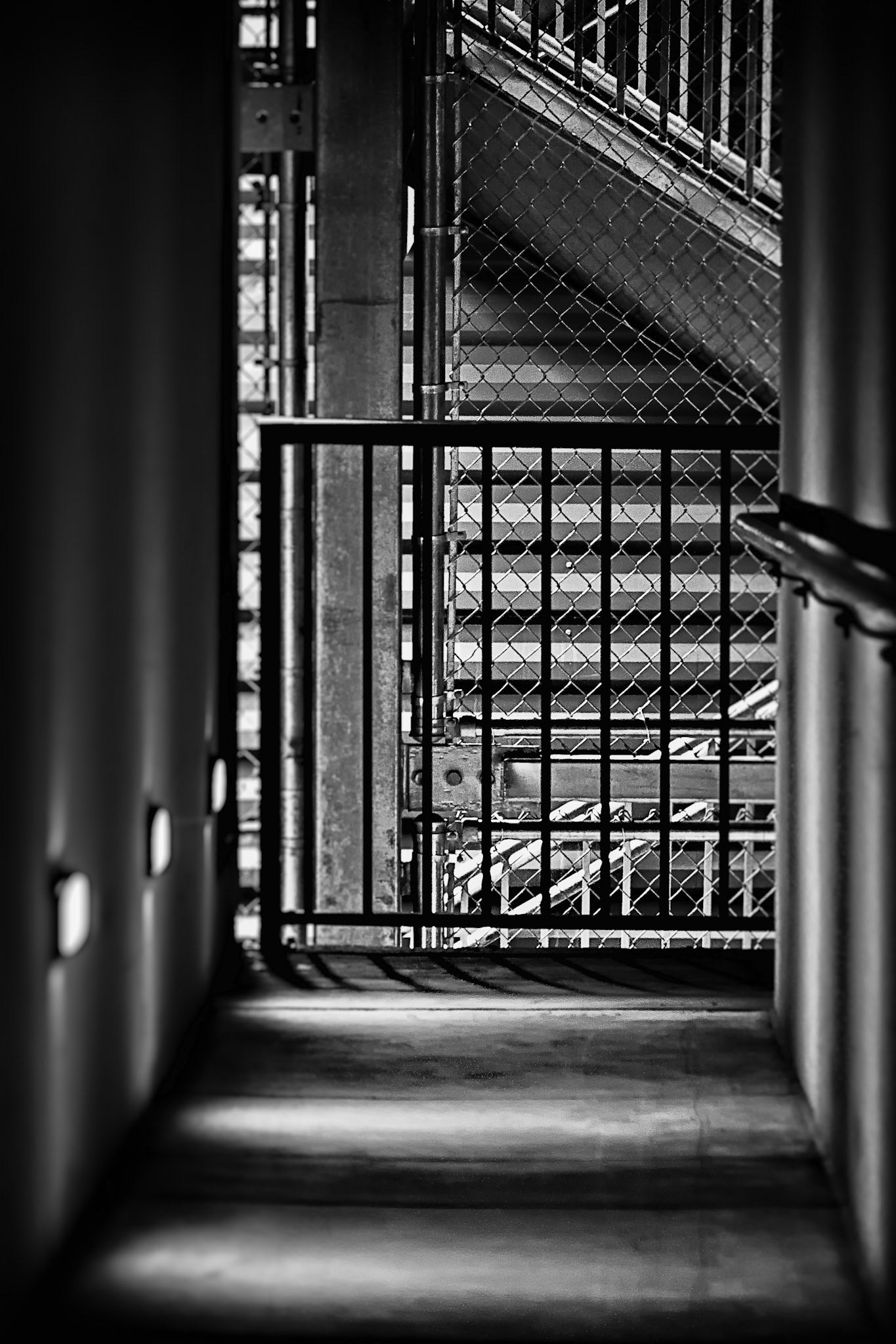 LINES OF PASSAGE  |  Cities often reveal themselves in unexpected places. Not in their landmarks or skylines, but in the overlooked spaces between destinations. This narrow passage, framed by steel, concrete, and shadow, transforms a simple stairwell into a study of line, light, and geometry.What caught my eye was the rhythm of the scene. Repeating patterns intersect and overlap, while shafts of light spill across the floor, creating a quiet sense of order amid the complexity of the urban environment. The image feels both industrial and architectural, revealing a hidden beauty in a place most people would walk past without a second glance.As a photographer, I am drawn to these anonymous spaces. They remind me that compelling images are not always found at the end of a journey. Sometimes they are waiting in the corridors we pass through every day.
