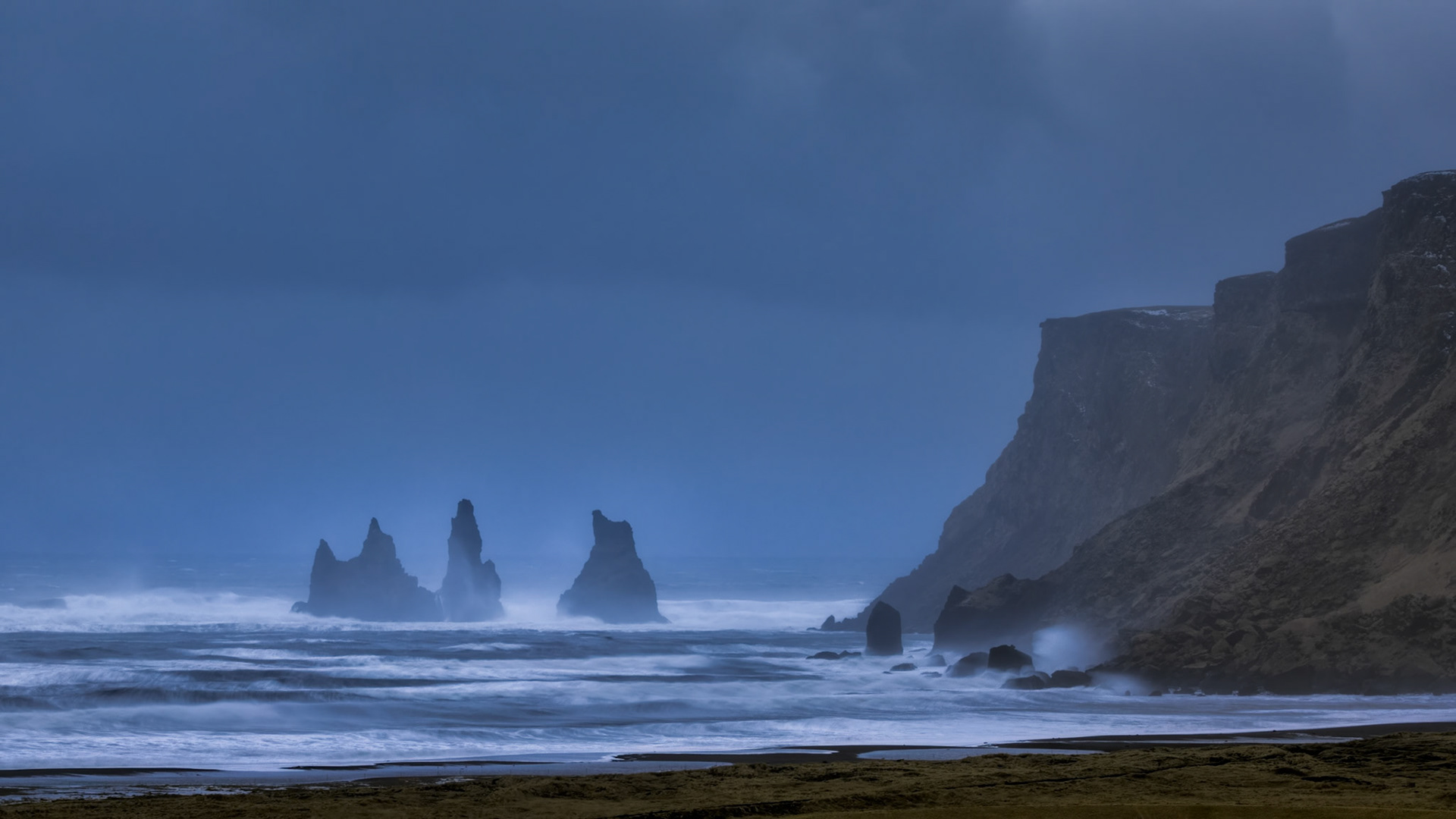 SENTINELS IN THE STORM  |  Iceland's famous black sand beaches are beautiful from a distance, but on days like this they remind visitors who's in charge. Powerful winds swept across the shoreline, lifting volcanic sand into the air and turning a simple walk into an exercise in endurance.The sea stacks of Reynisdrangar emerged through the mist as waves crashed against the coast and blowing sand stung exposed skin. The conditions were harsh, even punishing, yet undeniably captivating. It was a vivid reminder that Iceland's beauty is often inseparable from the raw forces that shape it.