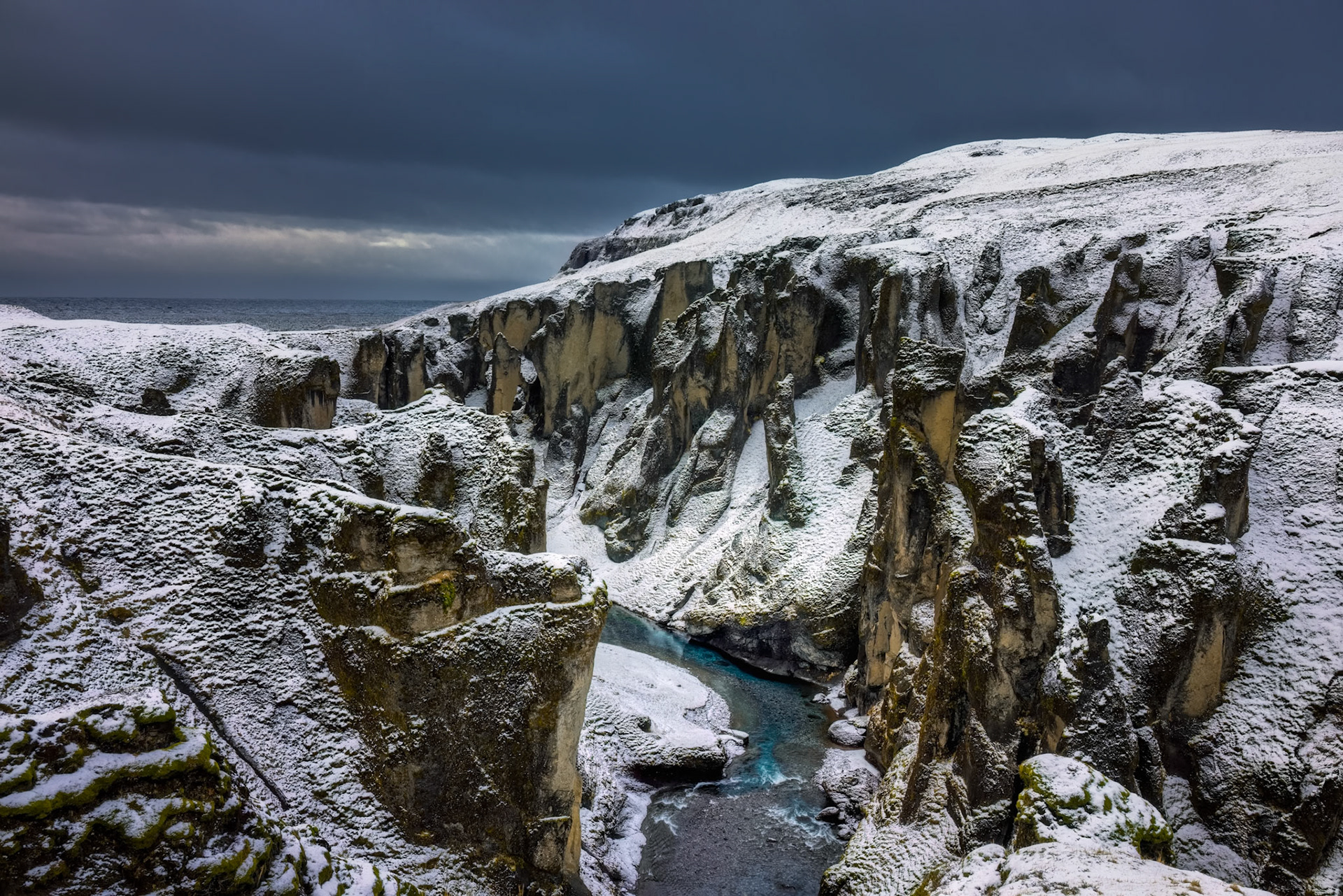 SILENT PASSAGE  |  **POWDERED WINTER**A light dusting of snow transformed this rugged Icelandic canyon into something almost ethereal. What only days before had been dark volcanic rock now appeared delicately coated in white, as though nature had sifted powdered sugar across every ledge, ridge, and spire.The contrast was mesmerizing. The turquoise river winding through the canyon seemed even more vibrant against the muted winter palette, carving its way through a landscape that felt both ancient and impossibly fragile. Every cliff face revealed new textures, softened by snow yet still shaped by centuries of wind, water, and volcanic forces.What struck me most was the sense of impermanence. The snowfall was light enough that a change in weather could erase it within hours. For a brief moment, however, this dramatic canyon exchanged its usual rugged character for one of quiet elegance, reminding me that even the wildest places can reveal an unexpected softness.