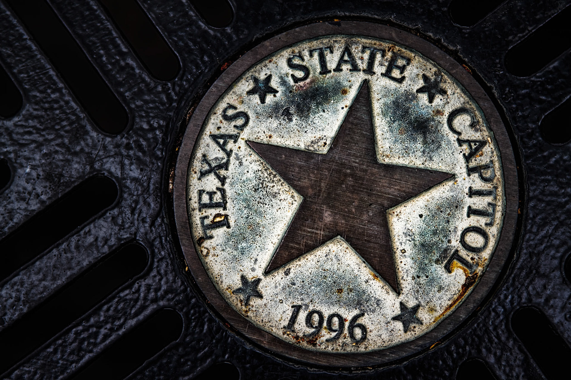 TEXAS UNDERFOOT  |  I found this Texas State Capitol emblem cast into a metal grate near the Capitol grounds. Years of weather and use have softened the surface, creating textures and patterns that contrast with the sharp lines of the Lone Star.What attracted me was the combination of history, symbolism, and wear. The star remains the focal point, while the surrounding metal shows the effects of time and exposure.It's a small detail that many visitors walk over without noticing, yet it carries one of the most recognizable symbols of Texas.