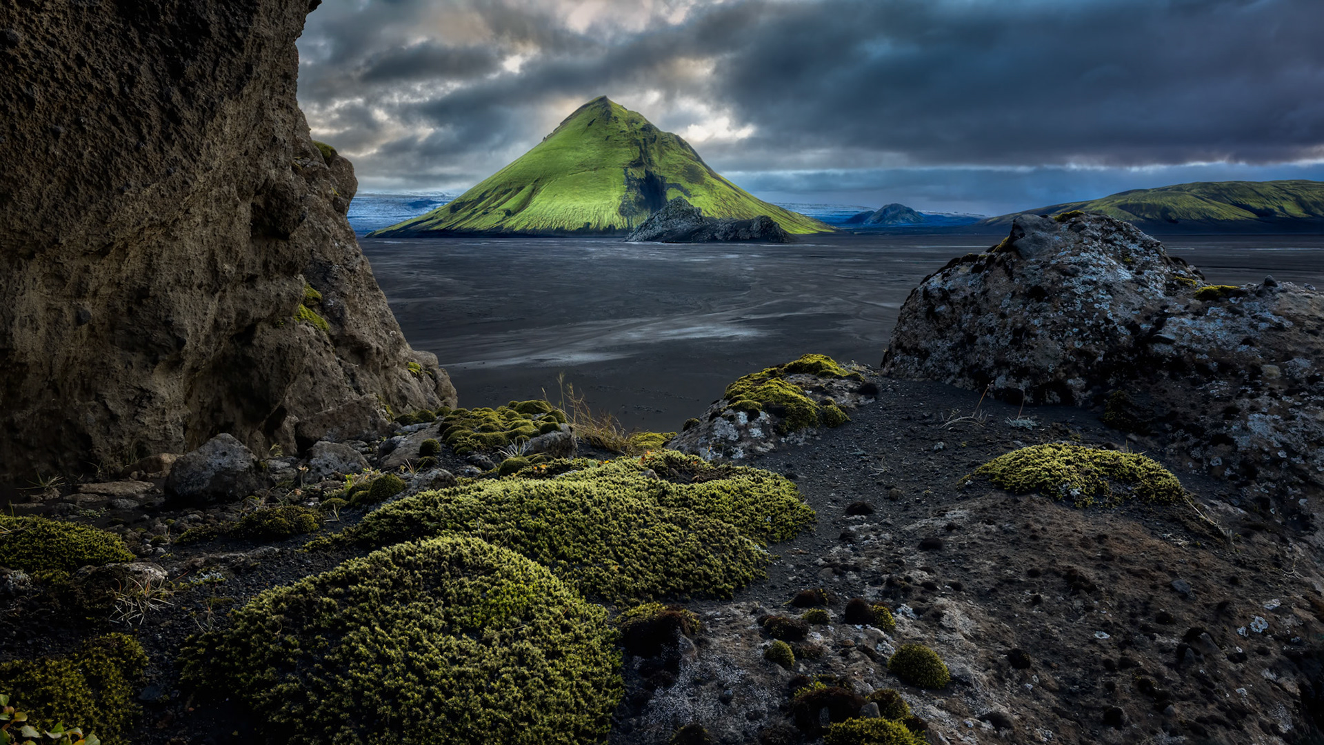GREEN CROWN OF THE HIGHLANDS  |  A shaft of sunlight breaks through the storm, illuminating a solitary green peak amid Iceland's vast volcanic highlands. Surrounded by black sands, ancient lava, and gathering clouds, the mountain glows like a beacon in an otherwise untamed landscape.