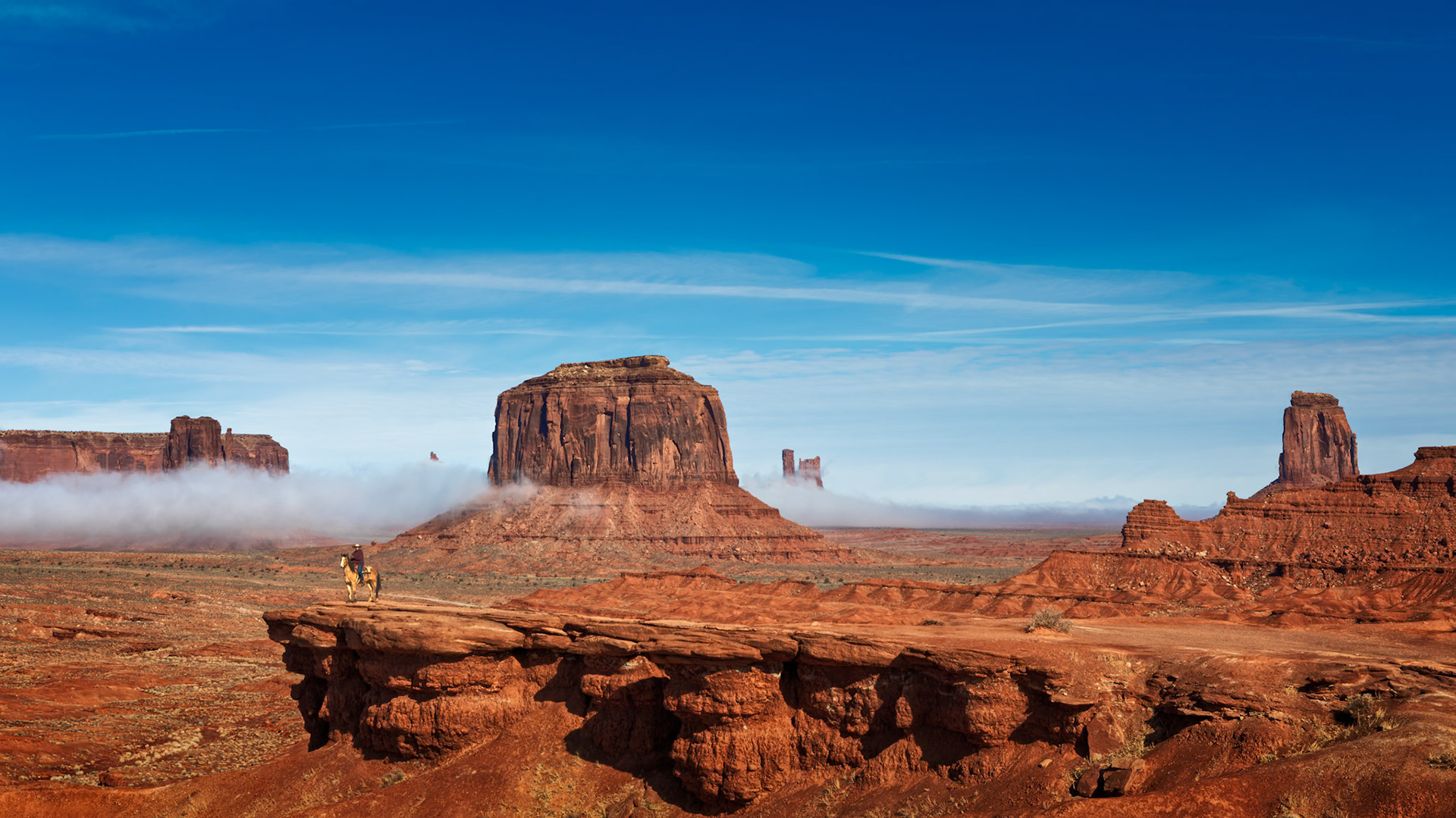 EDGE OF THE WEST  |  Monument Valley is often celebrated for its towering sandstone buttes, but on this morning my attention was drawn to something much smaller.A lone Navajo rider sat quietly on horseback at the edge of a rocky overlook, framed by one of the most iconic landscapes in the American West. Behind him, a low blanket of fog drifted across the valley floor, softening the horizon and adding an unexpected layer of mystery to the scene.What struck me most was the sense of connection.The rider wasn't simply in the landscape. He belonged to it.For generations, the Navajo people have called this remarkable place home. Long before it became known through movies, photographs, and travel brochures, these lands were woven into the history, culture, and daily lives of the people who lived here.As the morning light illuminated the red desert and the fog slowly dissolved into the distance, horse and rider seemed perfectly at ease, standing watch over a landscape that has changed little over countless generations.The scene felt timeless.Not a performance. Not a pose.Simply a quiet moment between a man, his horse, and the land that shaped them both.