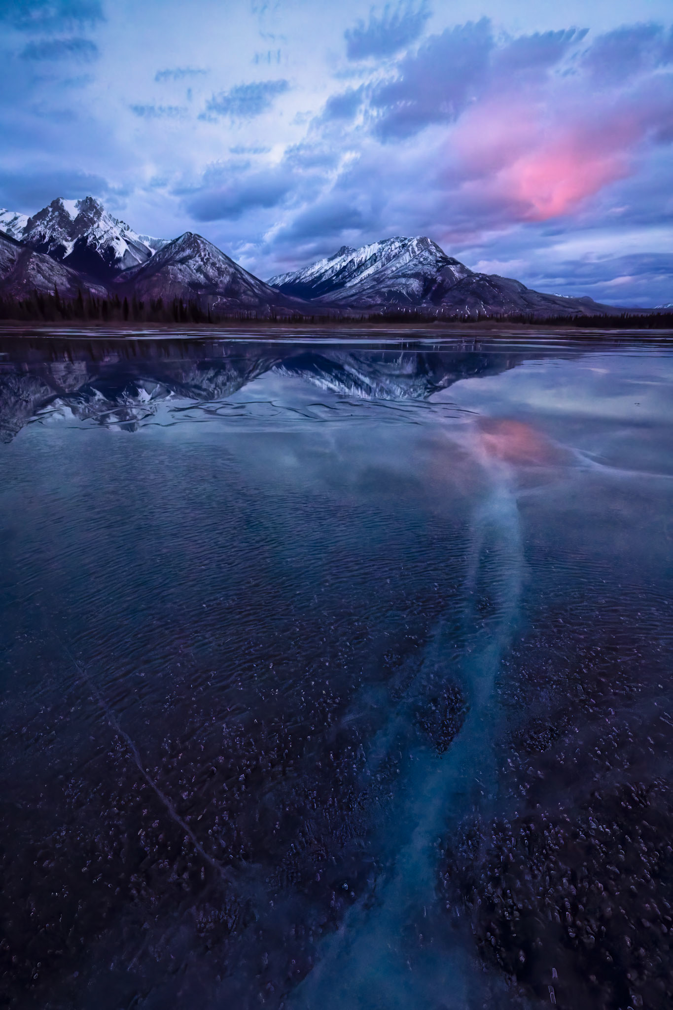 WHERE THE SKY COMES TO REST |  As dawn paints the Canadian Rockies in soft shades of blue and rose, the frozen lake becomes a mirror for the sky. For one quiet moment, earth and heaven seem to meet, inviting us to pause and simply breathe.