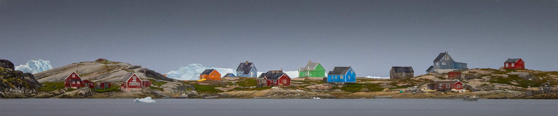 VILLAGE AT THE EDGE OF ICE  |  Life here exists at the boundary between permanence and change. Scattered across the rocky shoreline, brightly painted homes stand resilient against the vast Arctic landscape, their colors offering warmth and character beneath Greenland's muted skies.What makes this scene extraordinary is what lies beyond the village. Towering icebergs drift silently offshore, reminders that one of the world's most active glaciers is never far away. For the people who live here, the presence of ice is not a spectacle. It is part of everyday life.I was drawn to the contrast between the small scale of the settlement and the immense forces surrounding it. The homes appear almost fragile against the ancient ice and weathered stone, yet they represent generations of endurance, adaptation, and community in one of the planet's most remote environments.  The panoramic format emphasizes both isolation and connection.