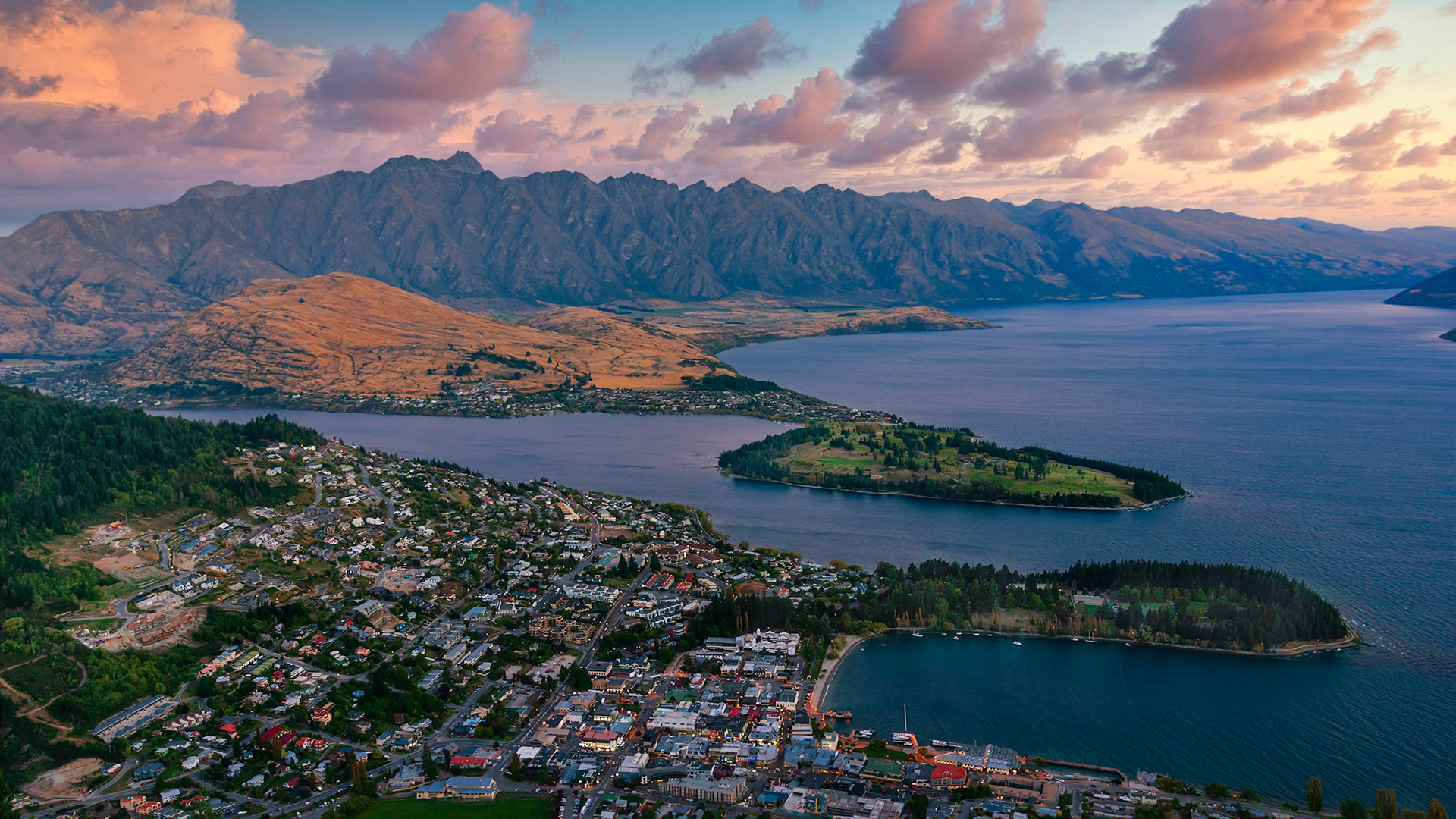 QUEENSTOWN, NEW ZEALAND  |  From high above Queenstown, the evening light reveals why this corner of New Zealand has become legendary among travelers and photographers alike. Lake Wakatipu curves through the landscape like a ribbon of deep blue silk, while the rugged peaks of The Remarkables stand guard over the town below.As the sun slipped toward the horizon, the mountains caught the last warm light of the day, glowing amber beneath a sky brushed with soft pink clouds. The scene lasted only moments, yet it felt timeless. Looking across the lake, it was easy to understand why people travel halfway around the world to experience this view.For a photographer, these fleeting transitions between day and night are often the most rewarding. The light softens, colors deepen, and the landscape takes on a sense of quiet grandeur. Standing above Queenstown as dusk settled across the Southern Alps, I wasn't thinking about camera settings or composition. I was simply appreciating a beautiful view.