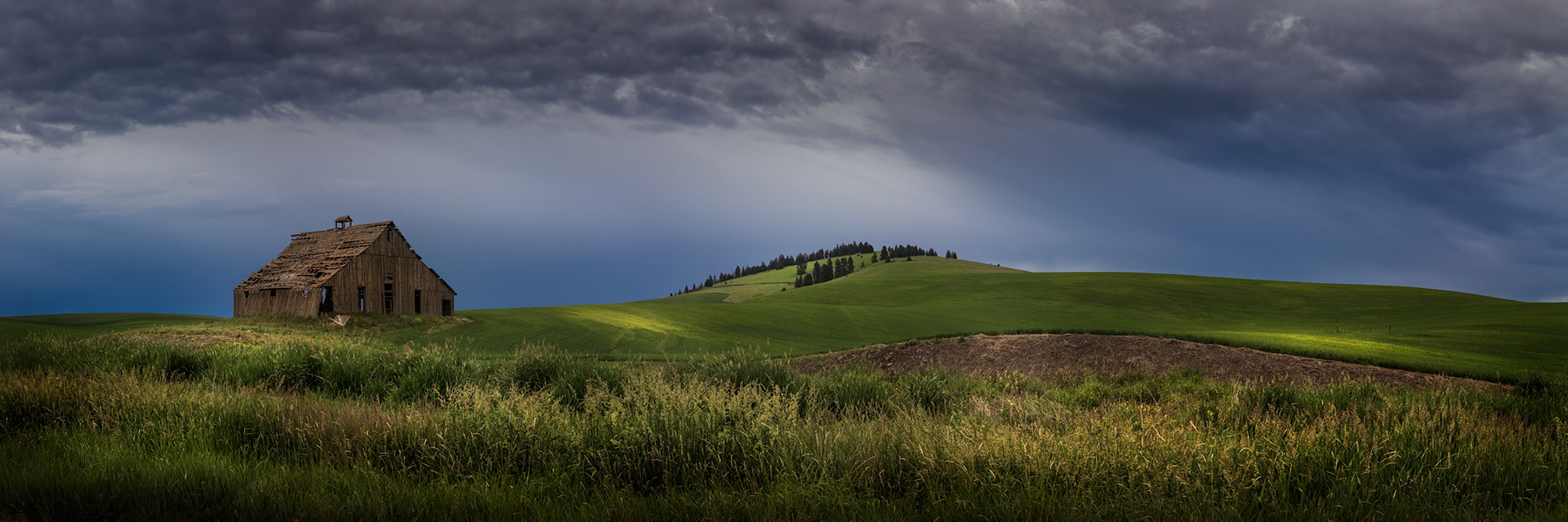 STORMLIGHT ON THE PALOUSE  |  A weathered barn stands alone beneath gathering storm clouds as sunlight briefly sweeps across the rolling hills of the Palouse. In a landscape shaped by wind, rain, and time, even the simplest scene can become extraordinary when the light arrives.