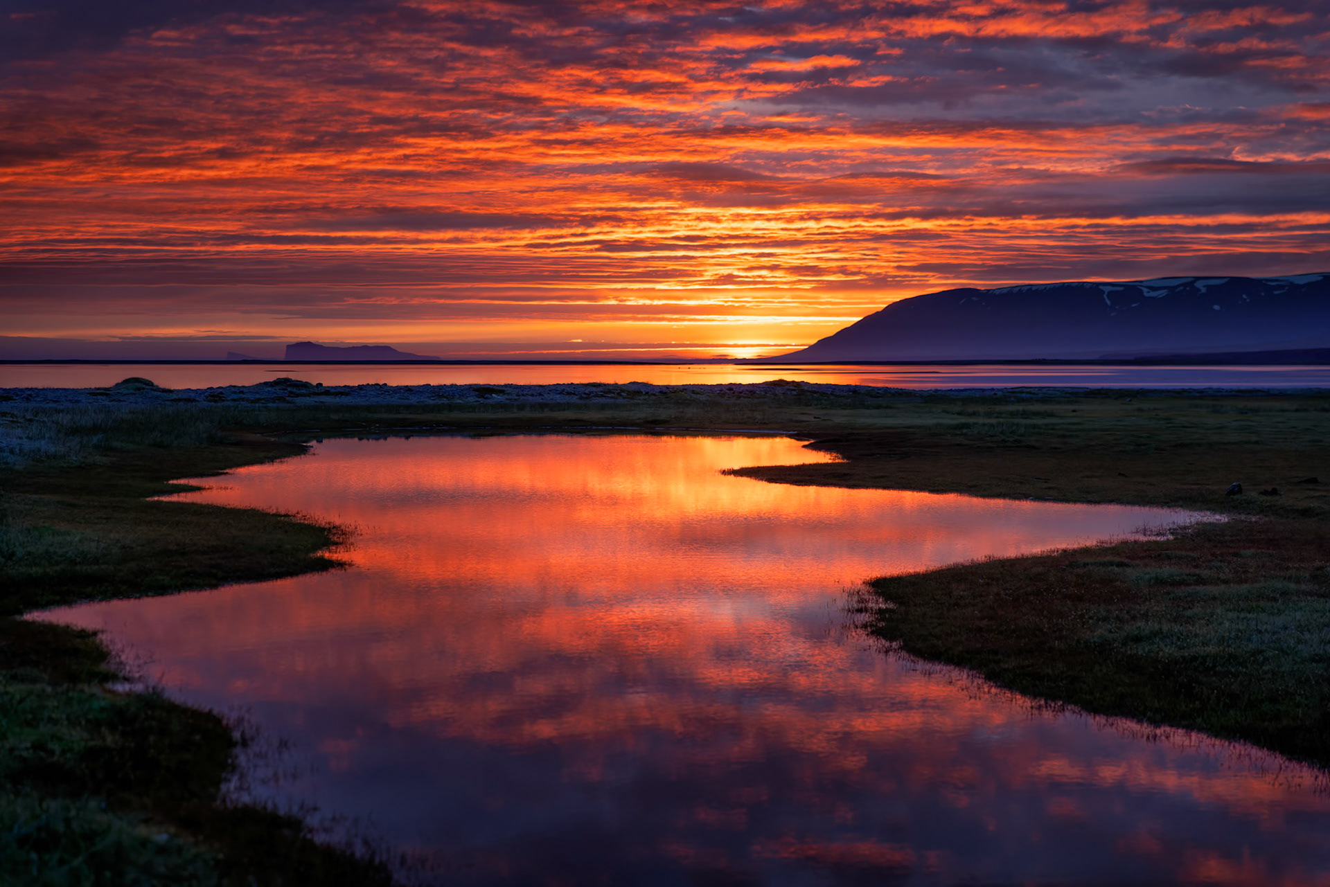 THE DAY'S LAST SECRET  |  At one o'clock in the morning, the sun still lingers just below the horizon, painting the Icelandic sky in brilliant shades of crimson, orange, and gold. The winding tidal channel mirrors the spectacle above, transforming a quiet landscape into a river of fire.