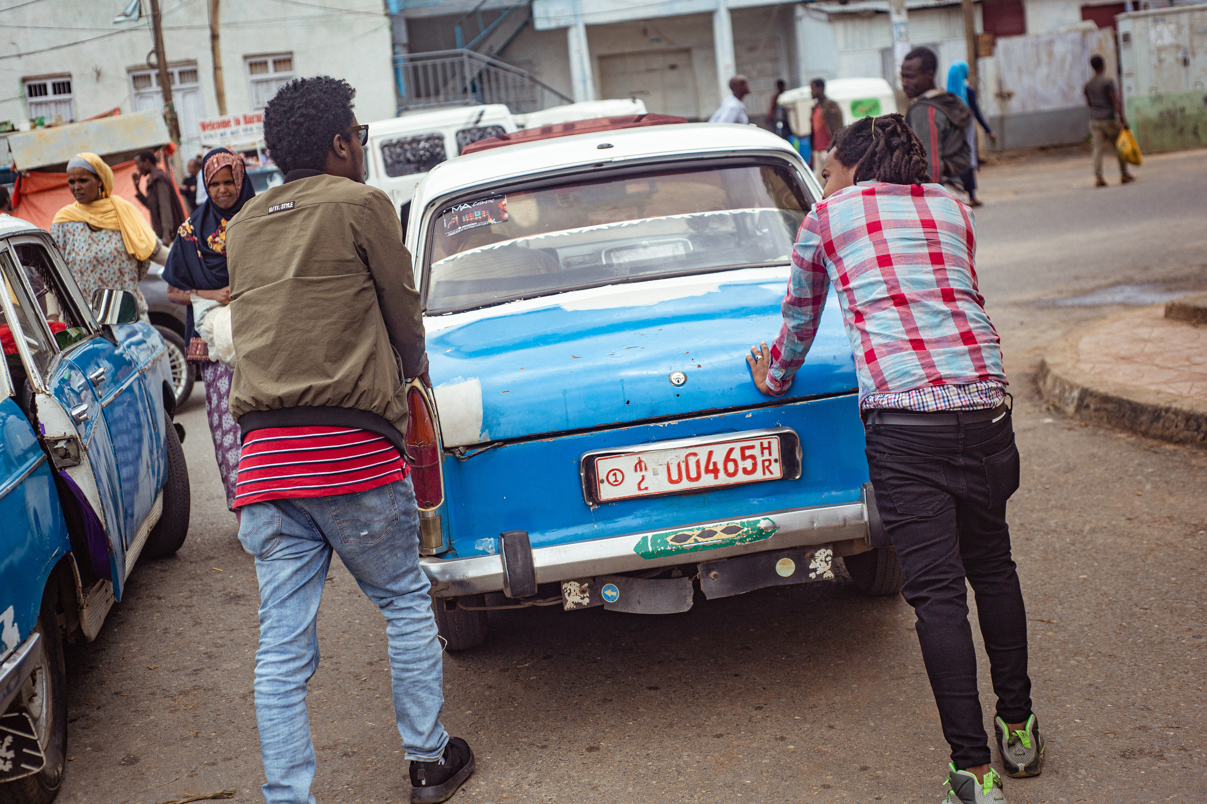 A driver enlists some bystanders to get his taxi going with a running start, a not too uncommon method with the vintage automobiles.