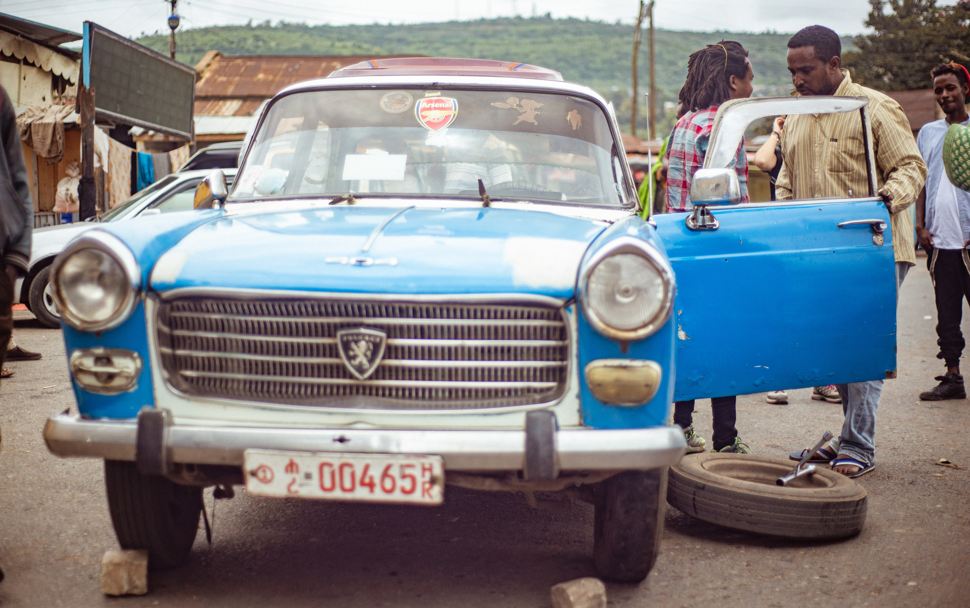 A driver changes a tire near the central roundabout. As most of the Peugeots are 50 to 60 years old, making repairs is a constant problem for drivers.