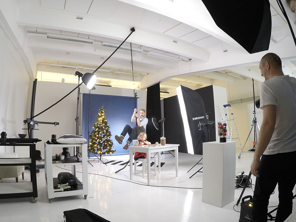 making-of photo from promotional shoot with small child making gingerbread and dad swinging from the ceiling