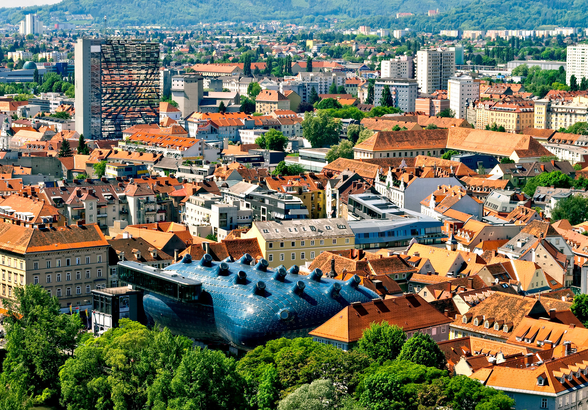 The Kunsthaus Museum in Graz. This gigantic building affectionately called the "Friendly Alien" by its creators Peter Cook and Colin Fournier, in form and material, stands out consciously against the surrounding baroque roof landscape with its red clay roofing tiles but nevertheless integrates the facade of the 1847 iron house.