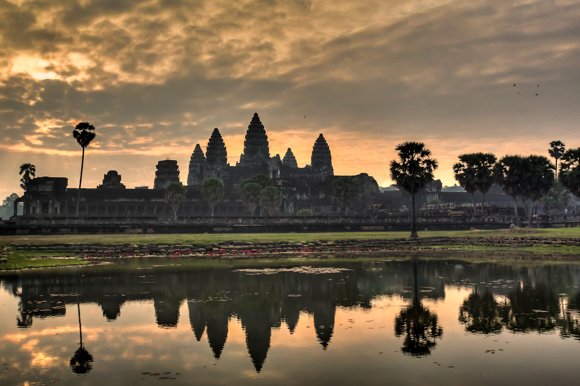 Angkor Wat is a temple complex at Angkor, Cambodia, built by King Suryavarman II in the early 12th century as his state temple and capital city. As the best-preserved temple at the site, it is the only one to have remained a significant religious centre since its foundation – first Hindu, dedicated to the god Vishnu, then Buddhist. The temple is at the top of the high classical style of Khmer architecture. It has become a symbol of Cambodia, appearing on its national flag, and it is the country's prime attraction for visitors. The modern name, Angkor Wat, means "City Temple".