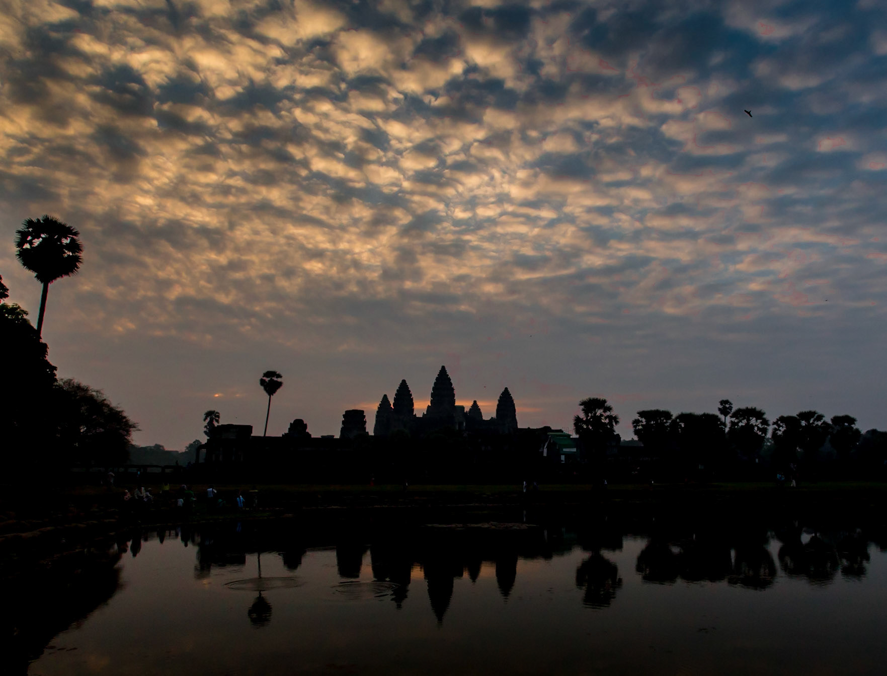 Angkor Wat is a temple complex at Angkor, Cambodia, built by King Suryavarman II in the early 12th century as his state temple and capital city. As the best-preserved temple at the site, it is the only one to have remained a significant religious centre since its foundation – first Hindu, dedicated to the god Vishnu, then Buddhist. The temple is at the top of the high classical style of Khmer architecture. It has become a symbol of Cambodia, appearing on its national flag, and it is the country's prime attraction for visitors. The modern name, Angkor Wat, means "City Temple".