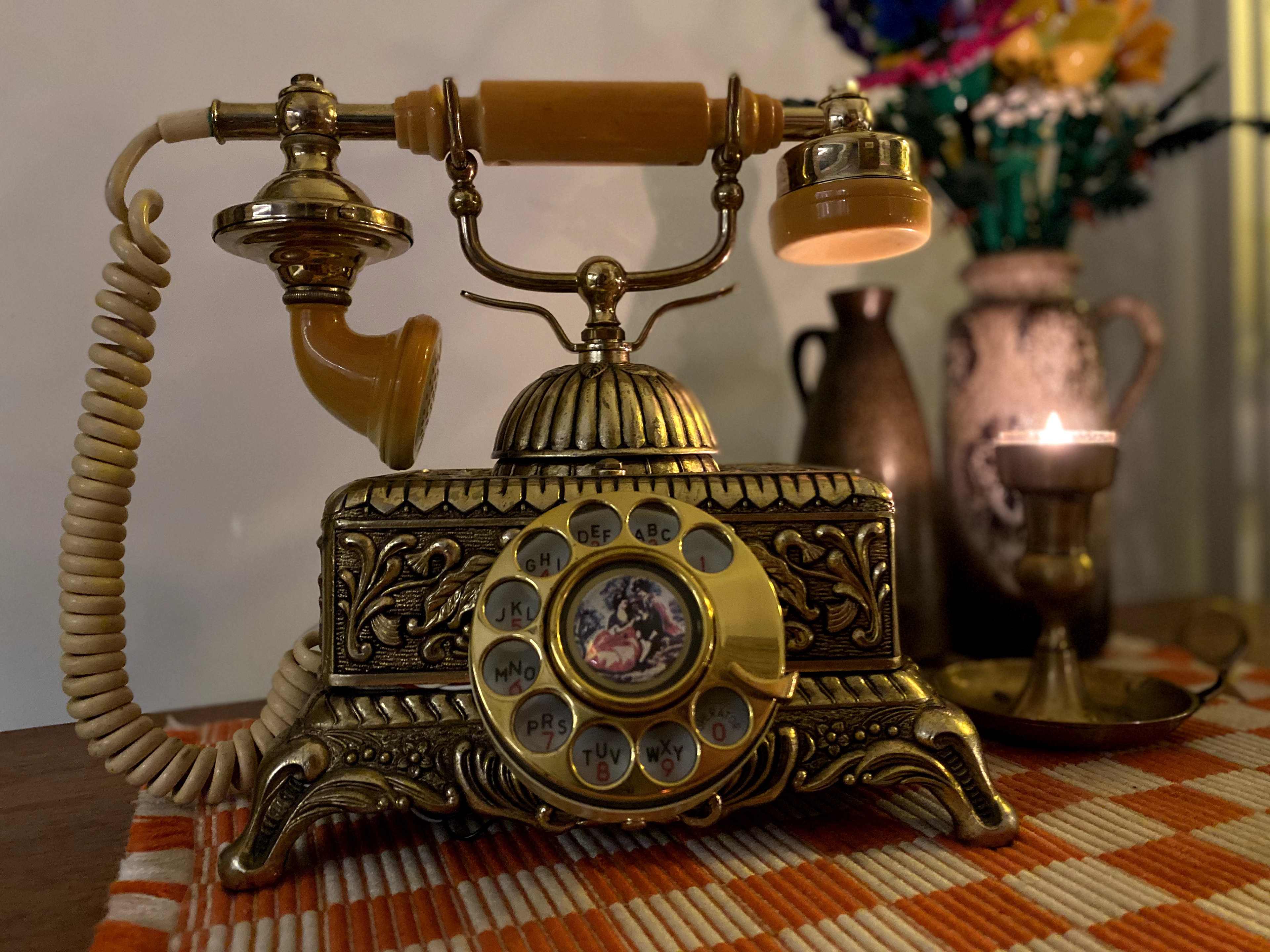 A vintage brass rotary phone next to a tea light and two vases