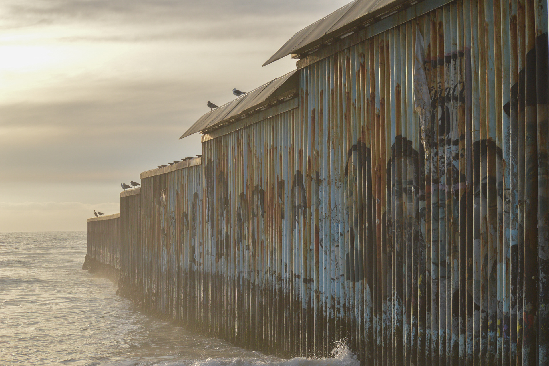 The U.S.-Mexico border wall meets the pacific ocean in Friendship Park. Faded murals of deportees adorn the Mexican side