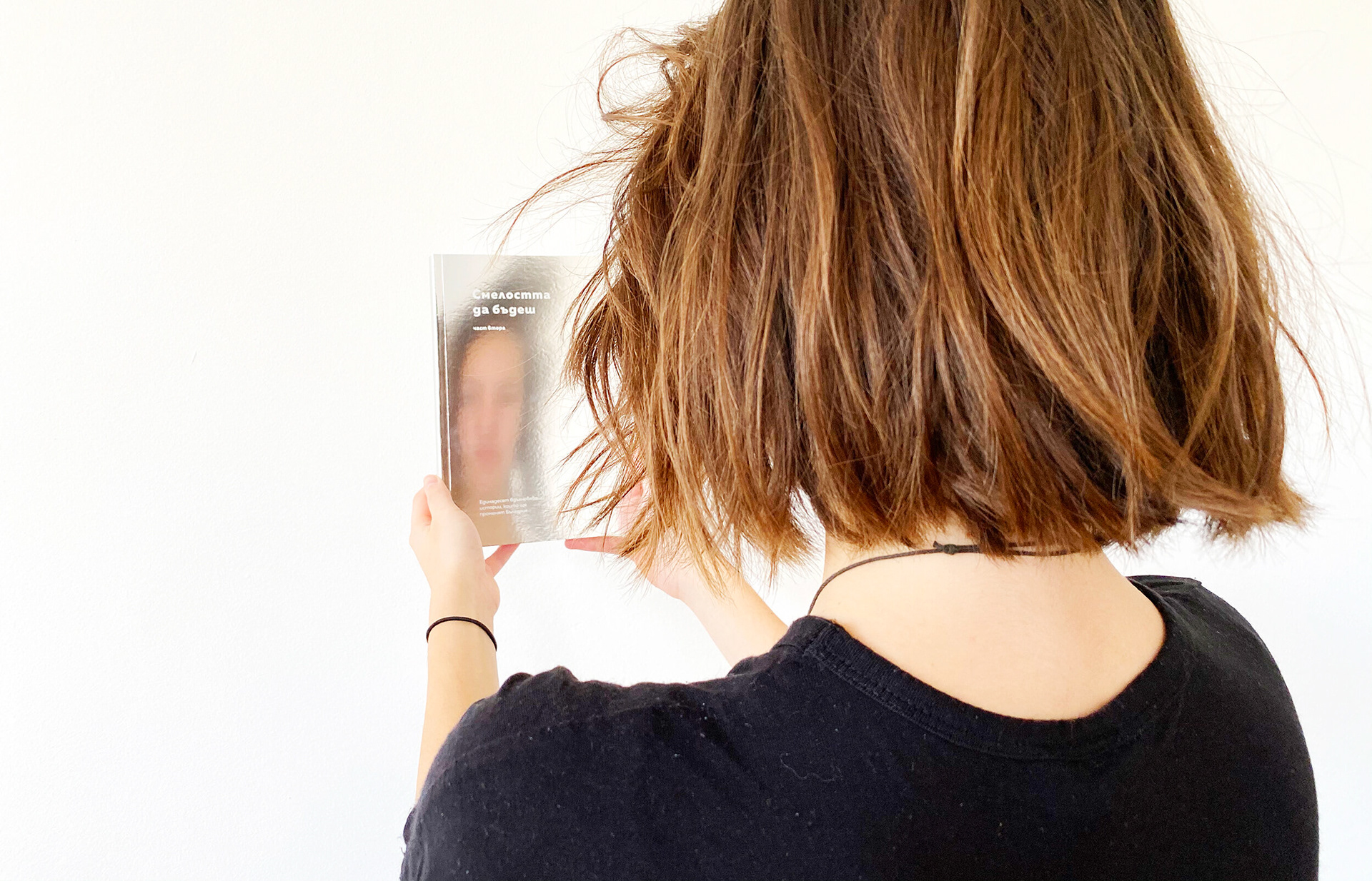 A girl holding the book. Blurred reflection of her face can be seen in the cover of the book