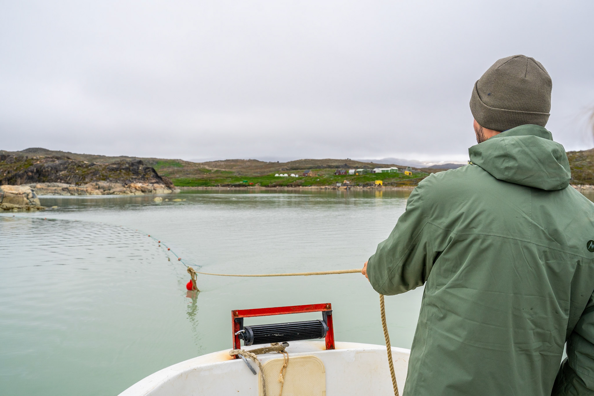 David pulling in a fishing net set out. Isortoq Reindeer Station visible in the background.
