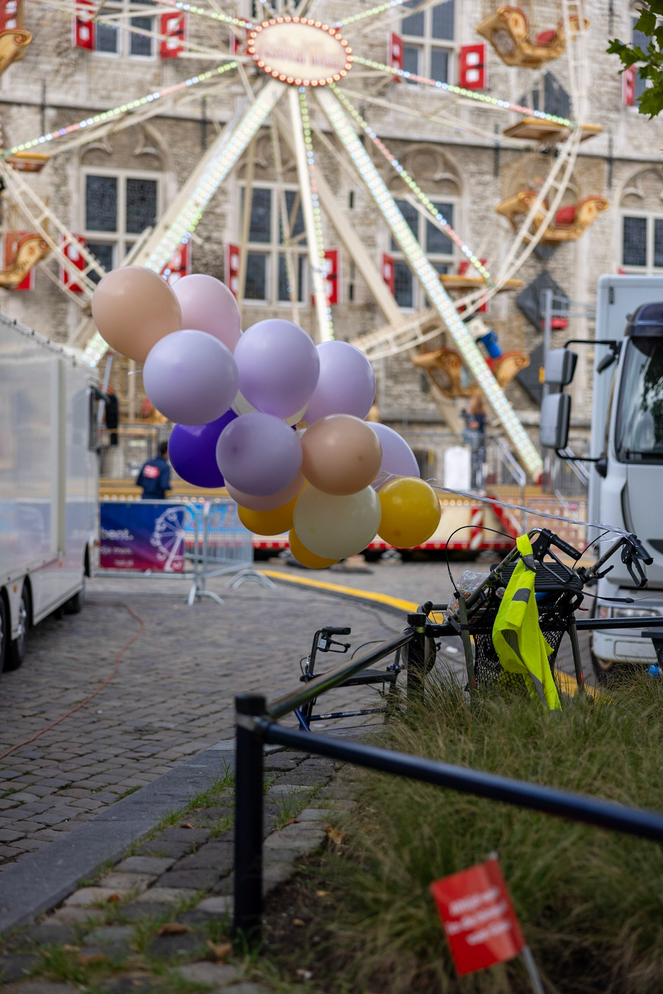 behind the attractions is hidden a walker with balloons. The Ferris wheel attracts people