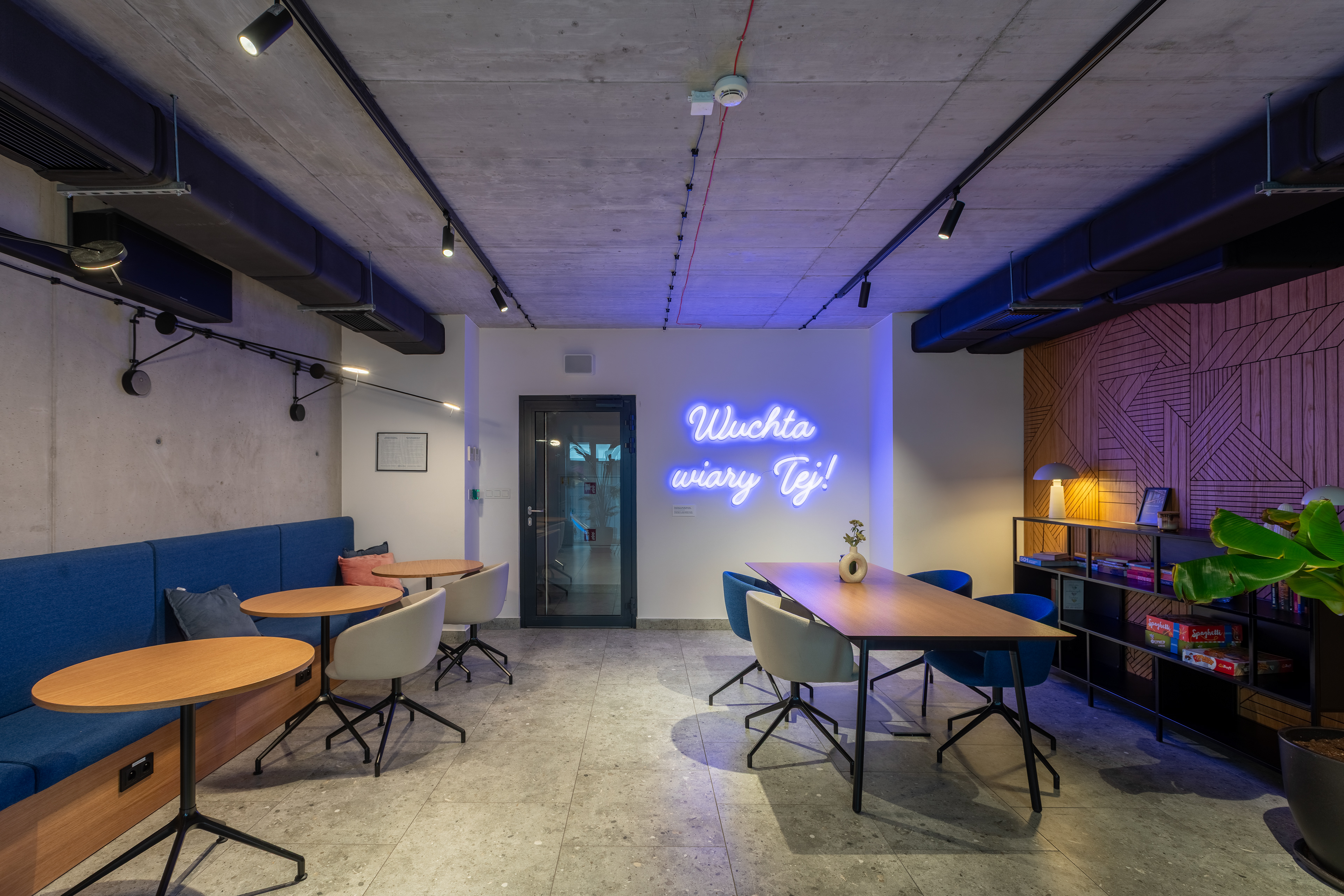 Strefa wspólna z okrągłymi stolikami i neonem – projekt ISA Architekci