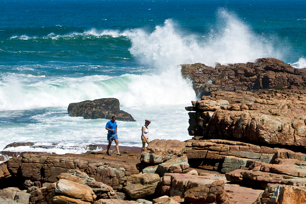 Zwei Besucher wandern am Kap der Guten Hoffnung, Südafrika. Wellen brechen im Hintergrund an den Felsen.