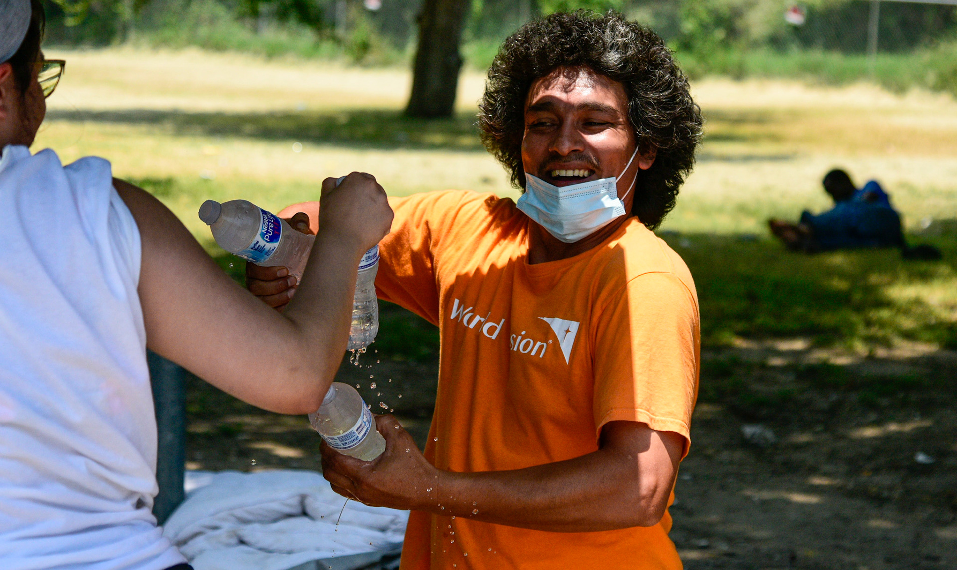 Volunteer Shelly Flores hands Carlos Pena water bottles provided by Feed the People Dallas at Our Calling, a discipleship ministry for the homeless, on June 18, 2021. Shot for The Dallas Morning News.