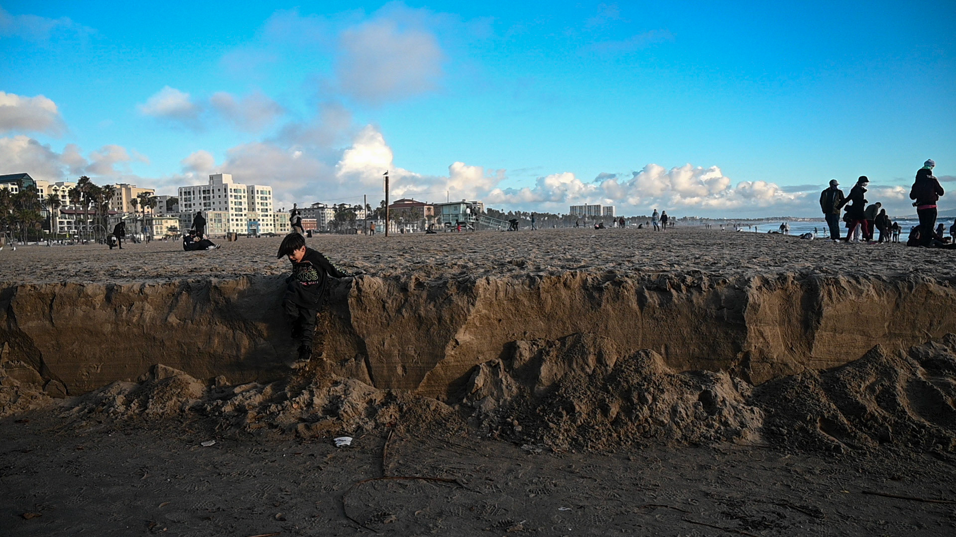 Tourists admire the water, boy enjoys the sand. 