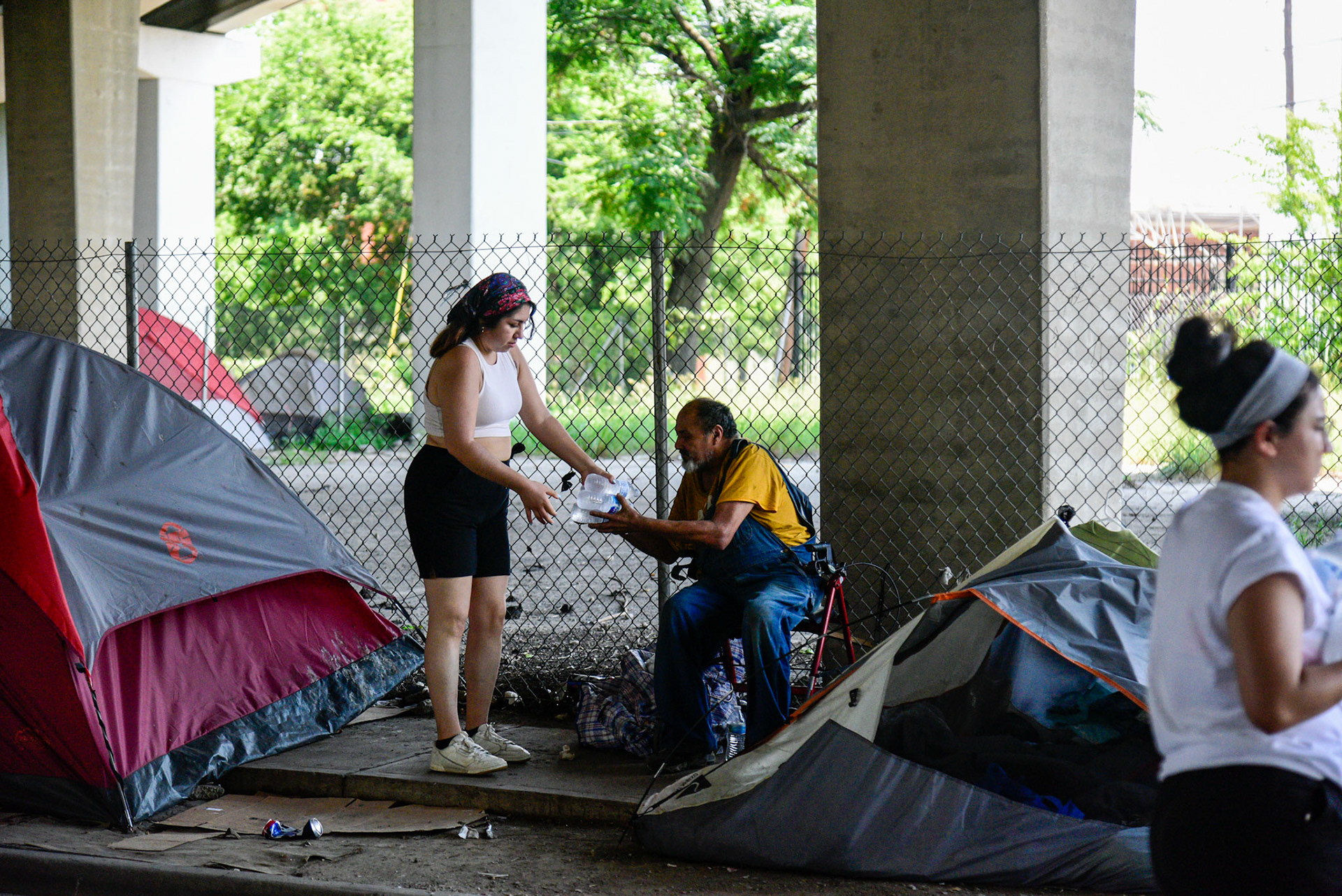 Volunteer Olivia Najera-Garcia hands out bottled water in under-freeway encampments for Feed the People Dallas on June 18, 2021.  Shot for The Dallas Morning News.
