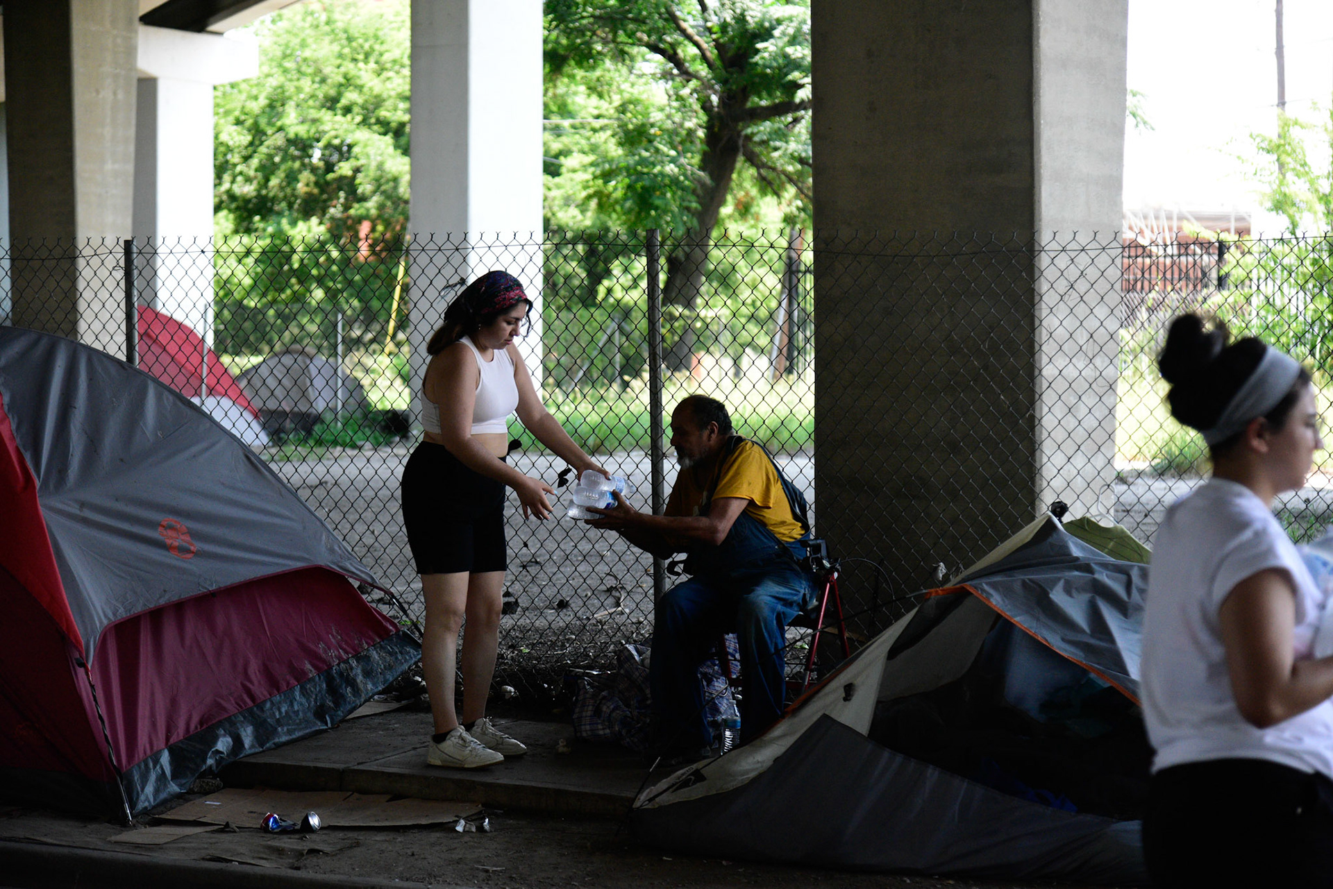 Volunteer Olivia Najera-Garcia hands out bottled water in under-freeway encampments for Feed the People Dallas on June 18, 2021.  Shot for The Dallas Morning News.