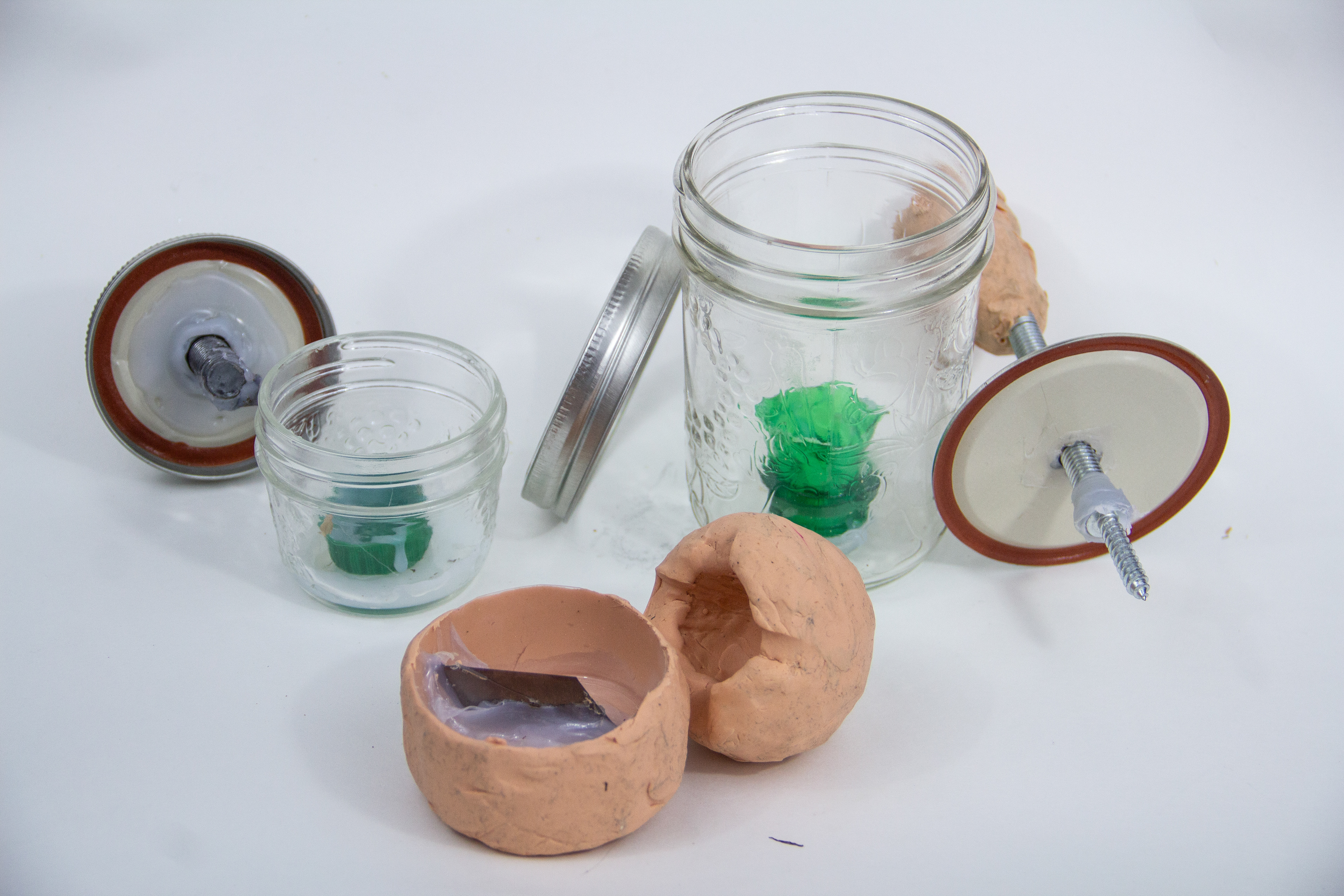 Walnut cracker prototypes: two glass Mason jars with mechanisms attached to the lids sit behind a plasticine prototype with a blade inside.