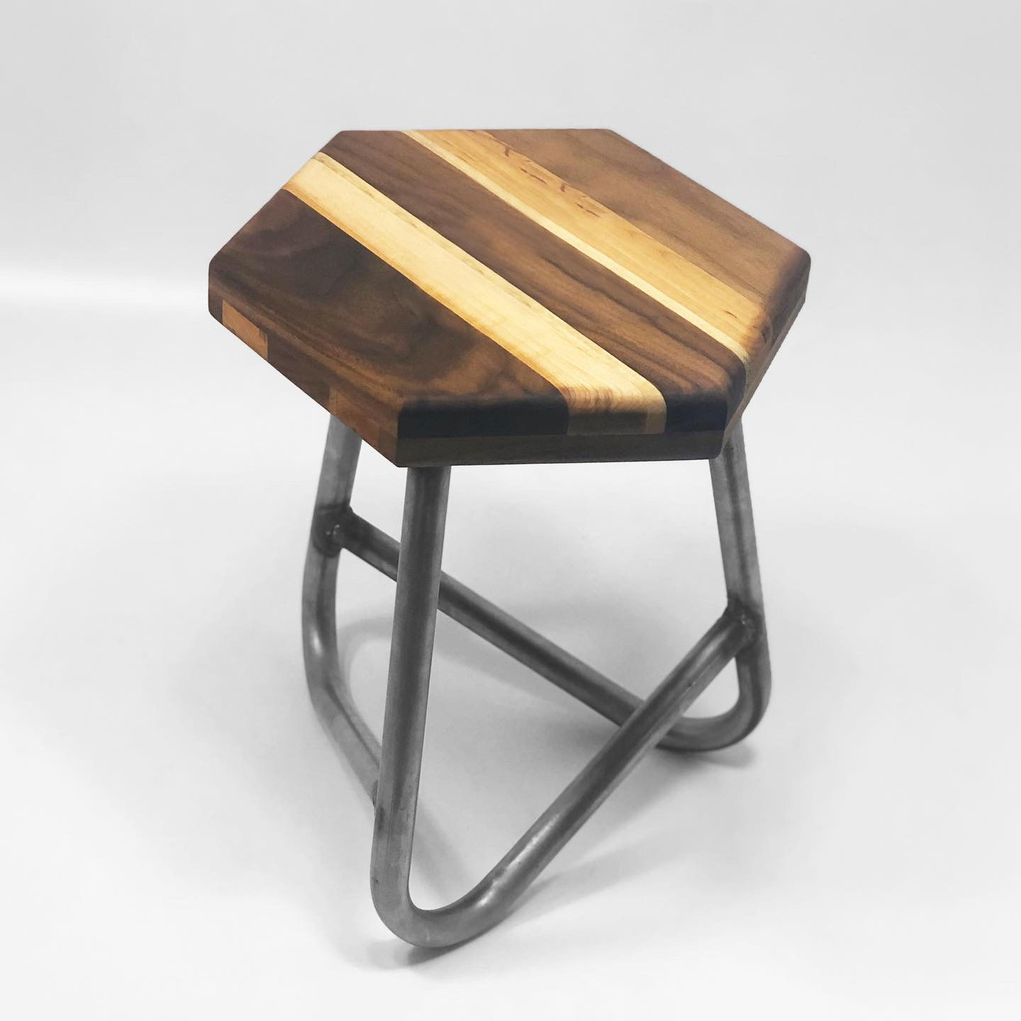 A hexagonal seat made of wood is held up with 3 bent tubes that make up the base of the stool. The stool sits on a white background.